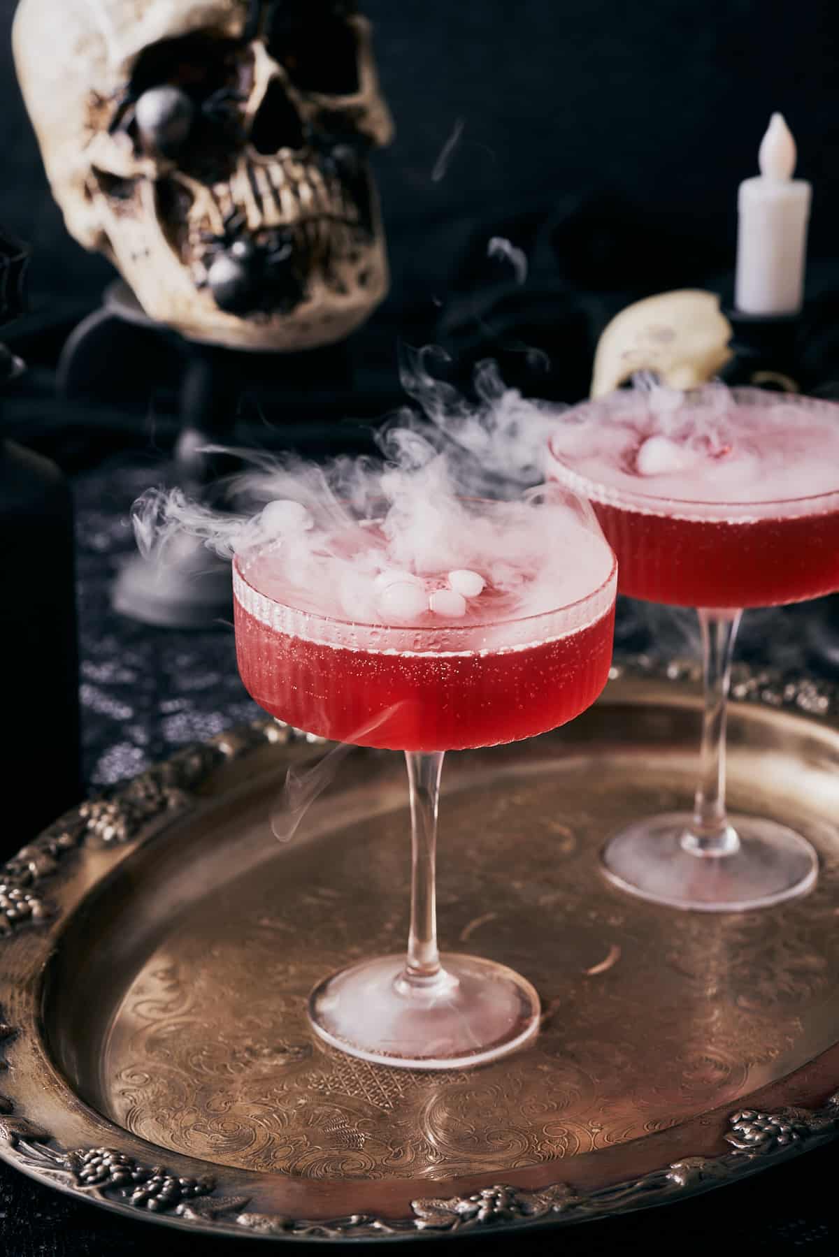 close up shot of two coupe glasses with red liquid, and dry ice coming out of the drinks. 