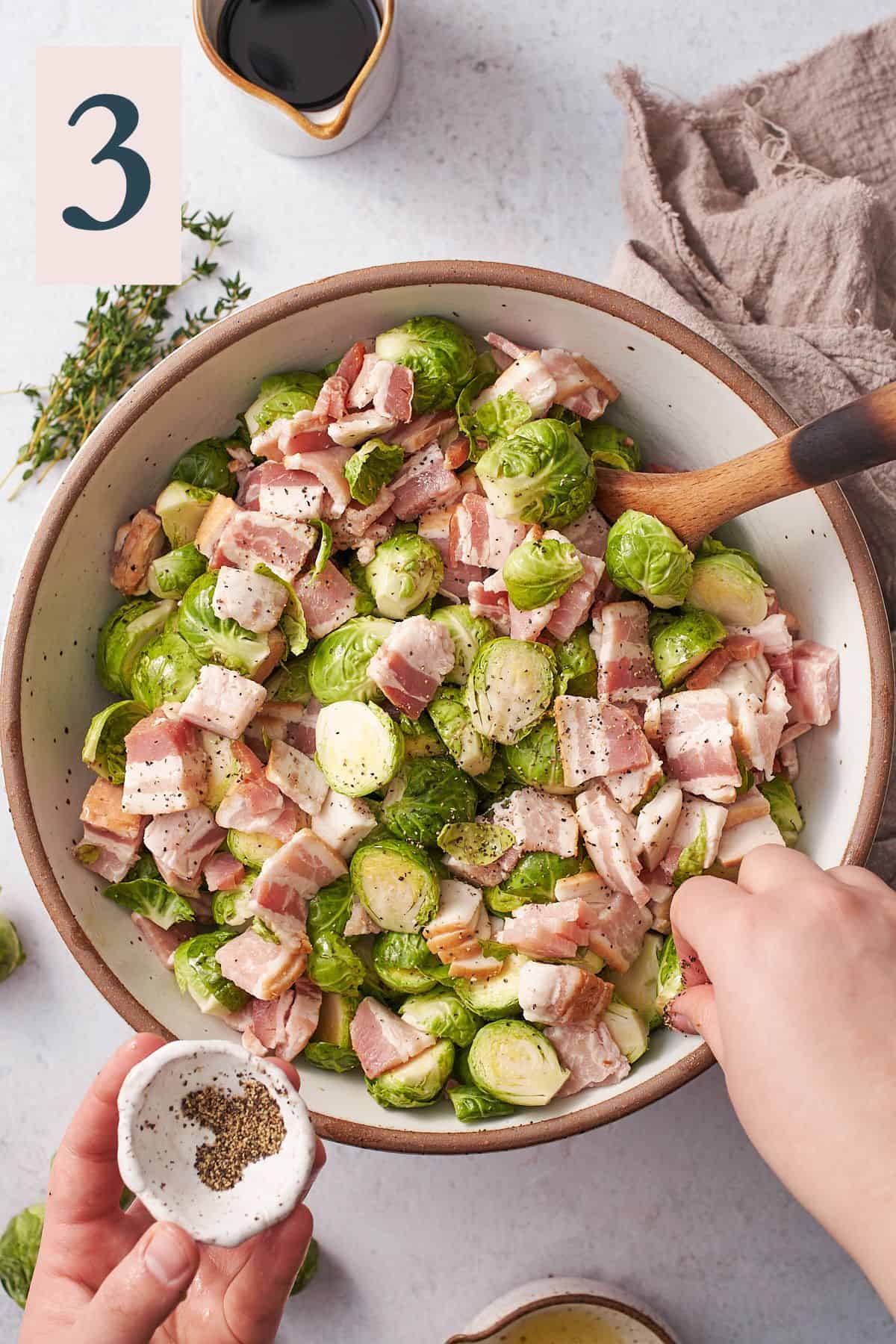 hand sprinkling black pepper into a bowl of brussel sprouts and raw bacon. 