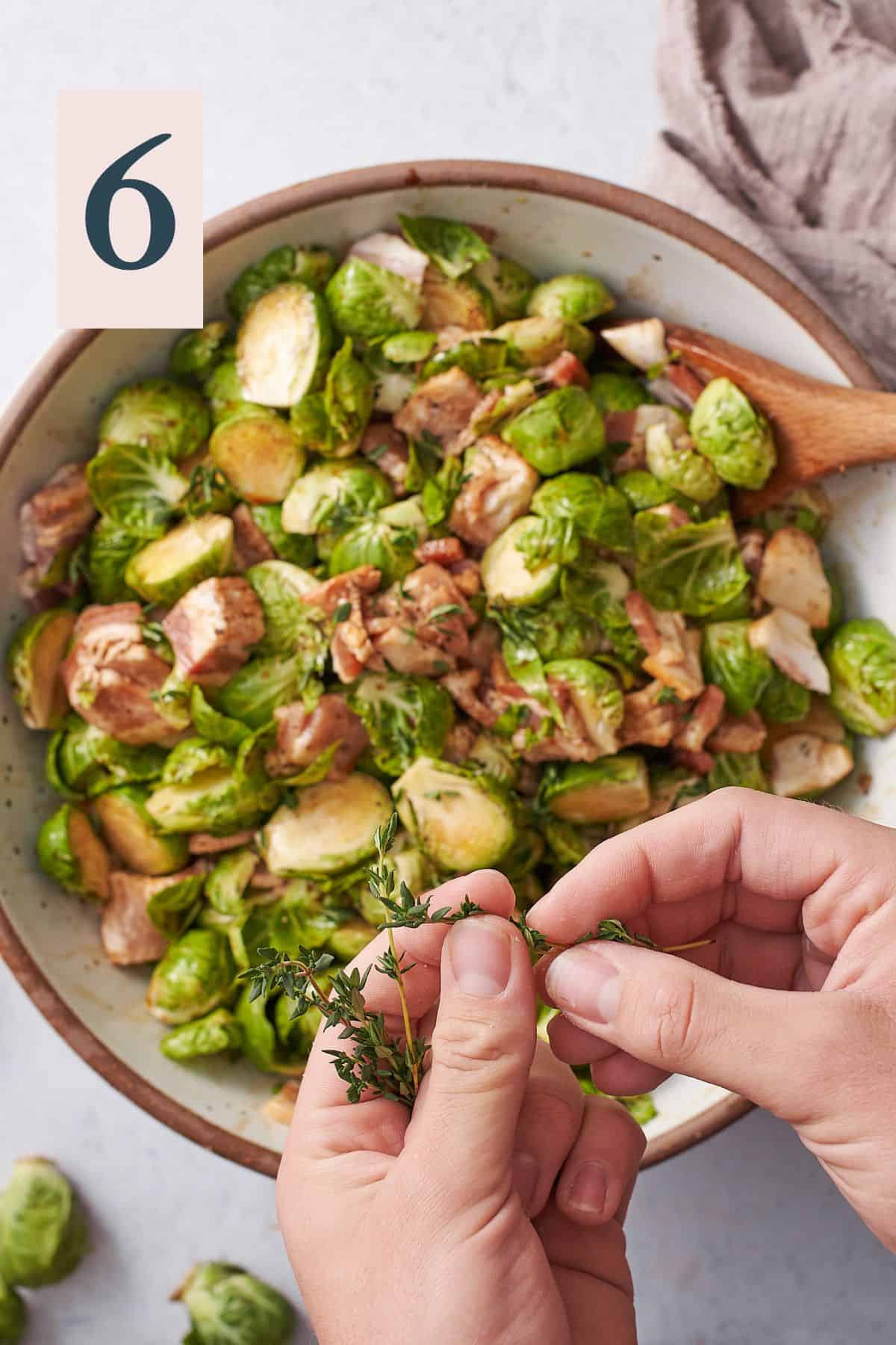 hand pulling leaves off of fresh thyme and placing them into a bowl of brussel sprouts and bacon. 