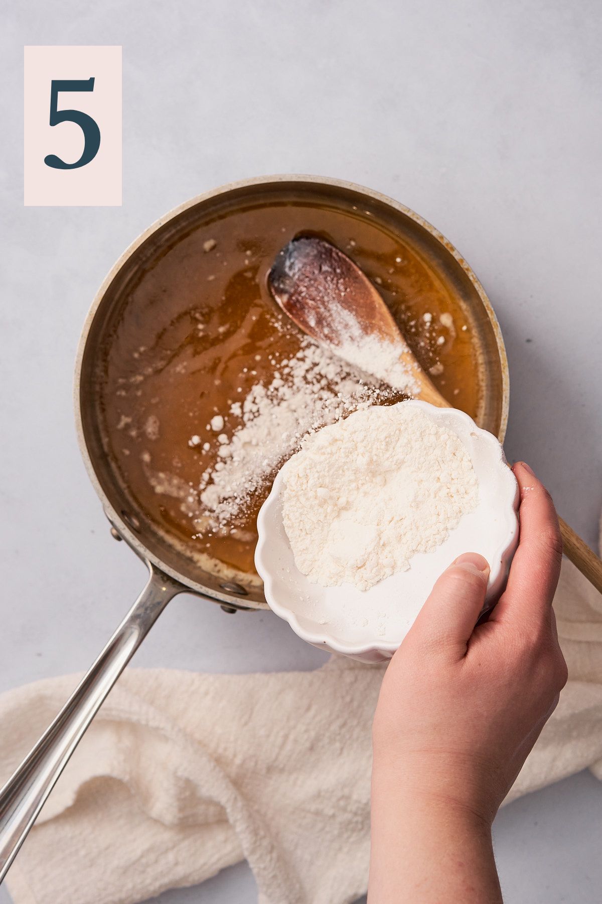 hand pouring in flour into a saucepan with melted butter.