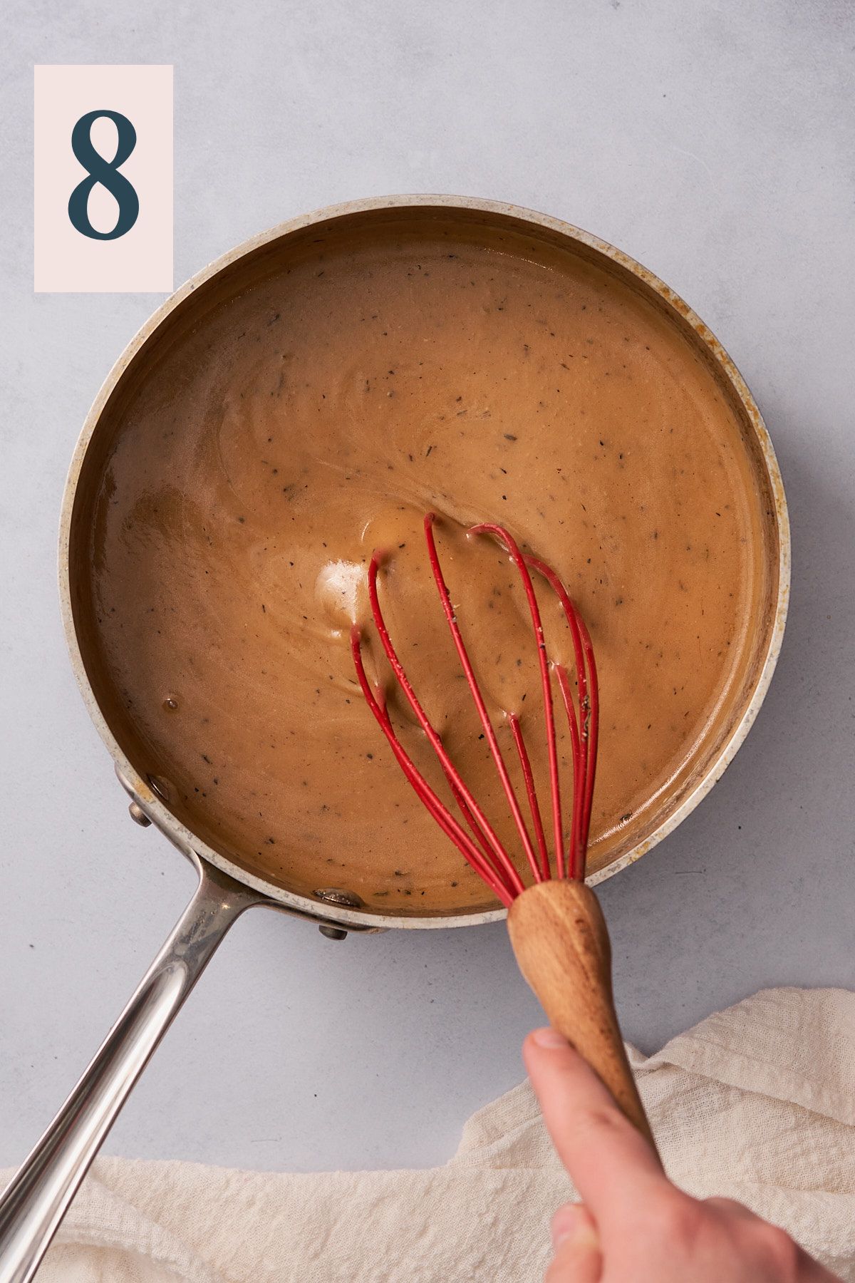 hand whisking turkey gravy in a small saucepan with red silicone whisk.