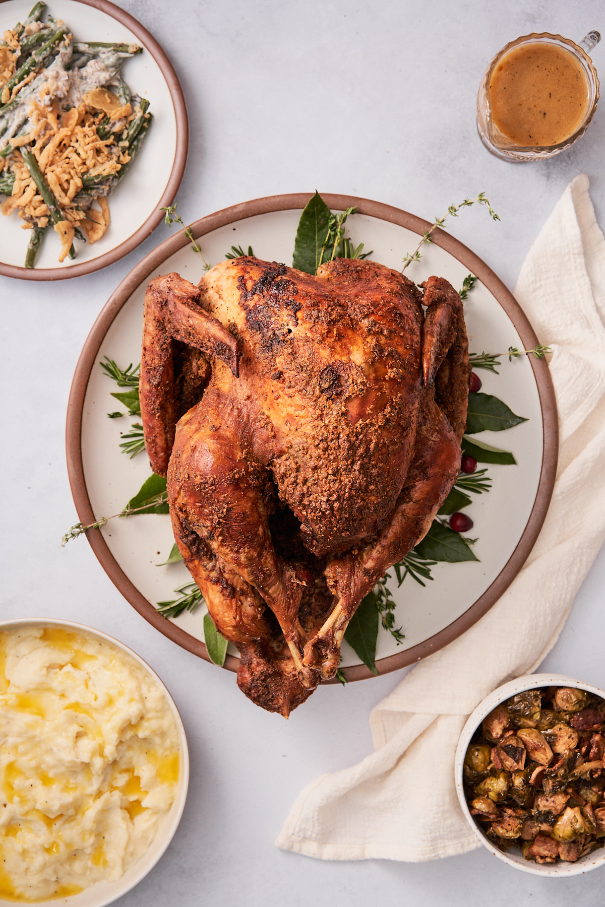 delicious whole roasted turkey on a round serving plate with bay leaves, thyme sprigs, fresh cranberries, and surrounded by side dishes. 