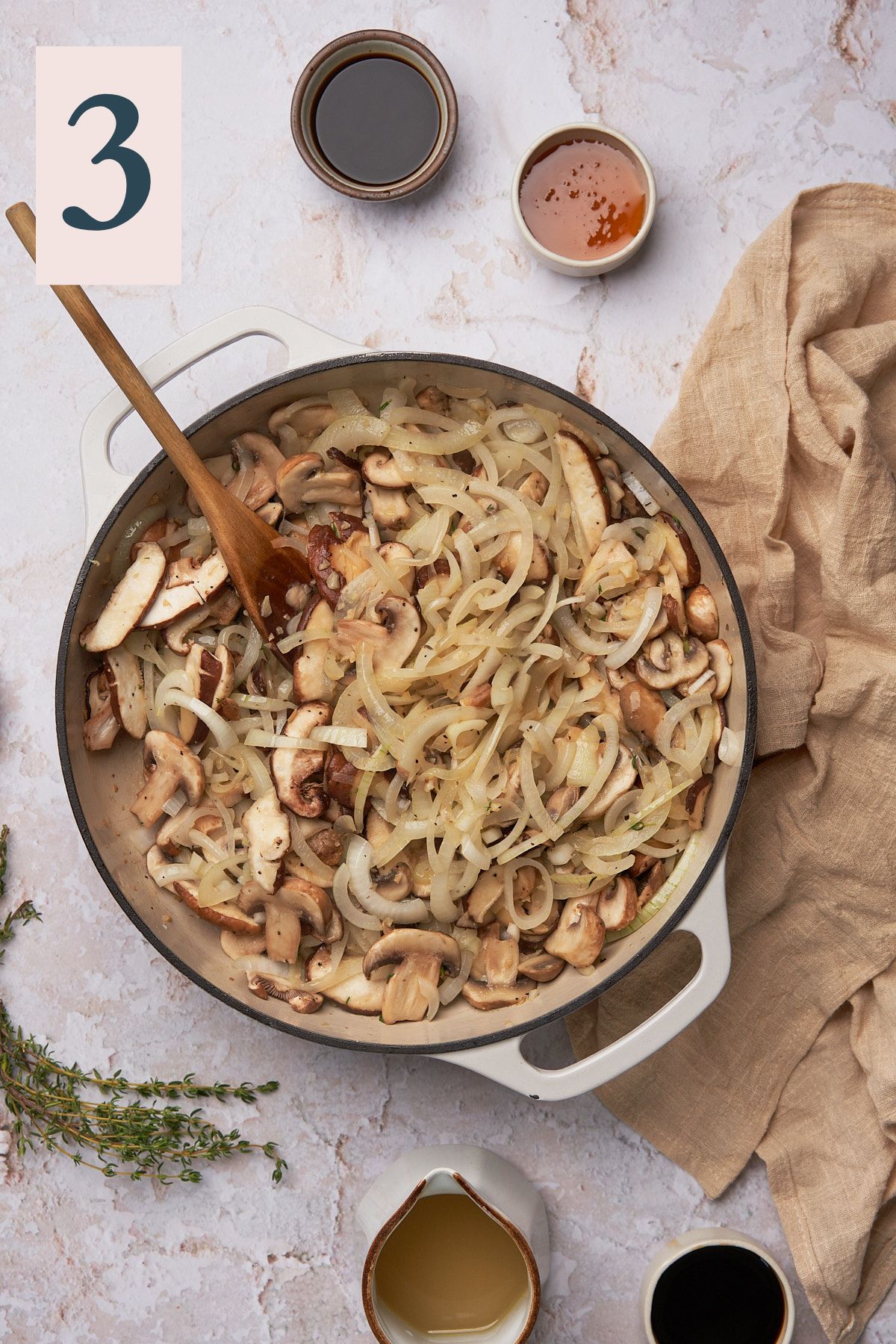 mushrooms and onions cooked down in an enameled cast iron skillet with a wooden spoon.