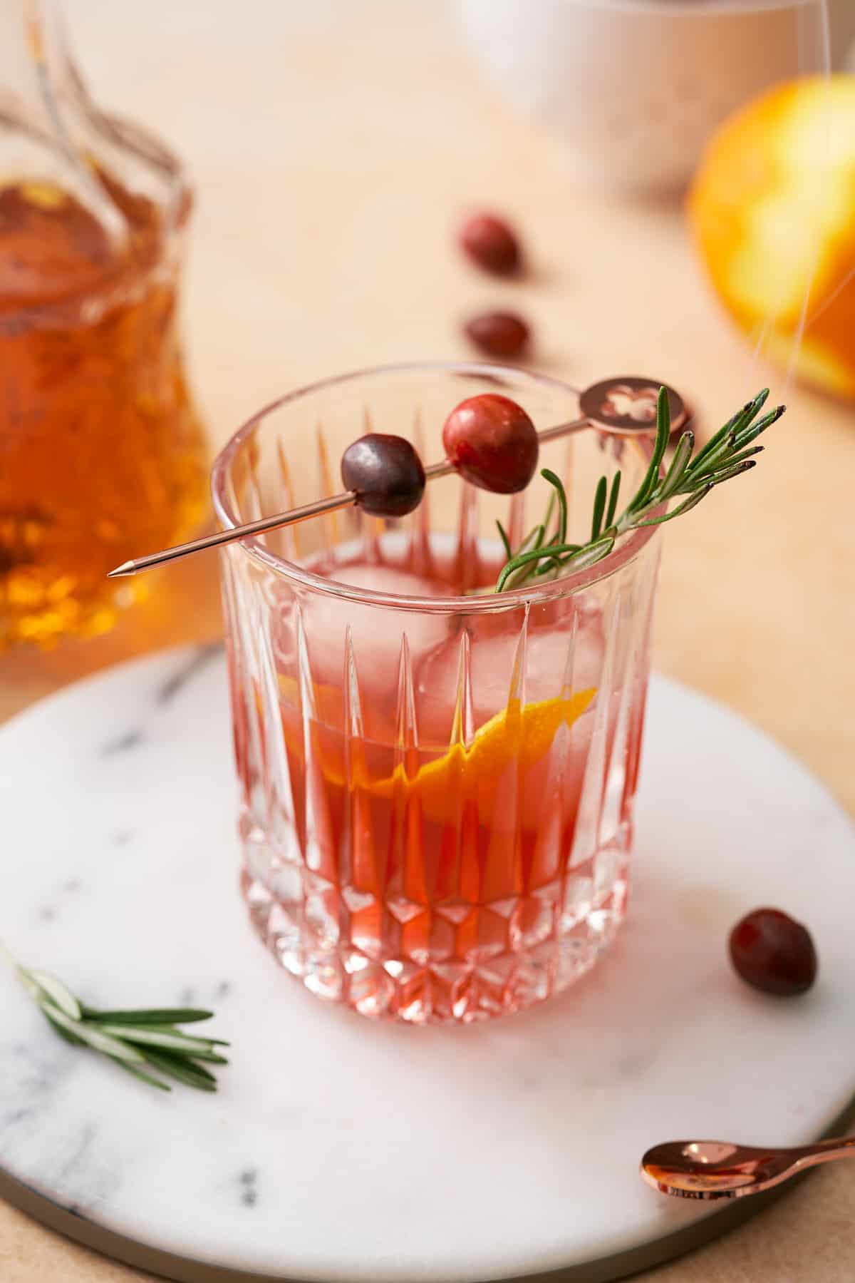 stunning cranberry old fashioned in a decorative rocks glass, with rosemary, fresh cranberries, and an orange peel. 