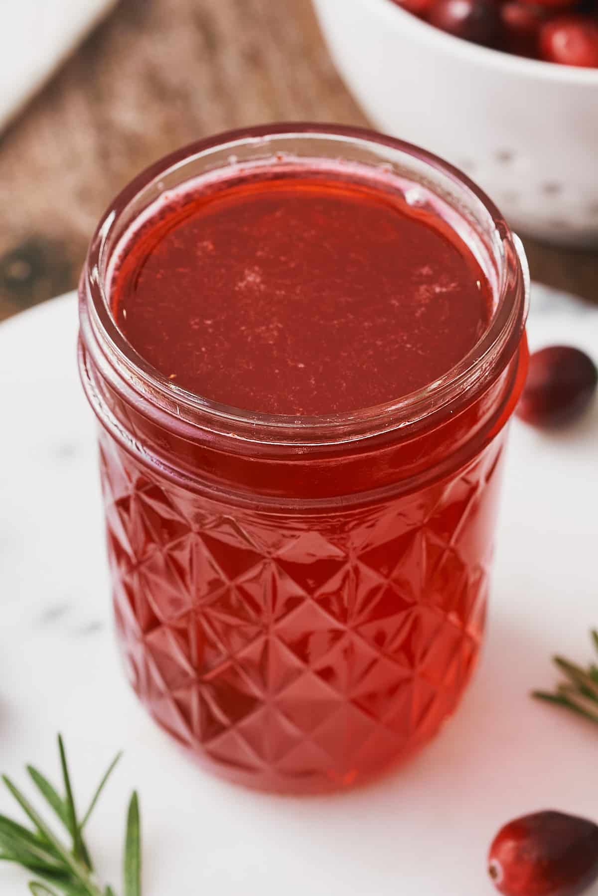 close up shot of a small mason jar filled with bright red cranberry simple syrup. 