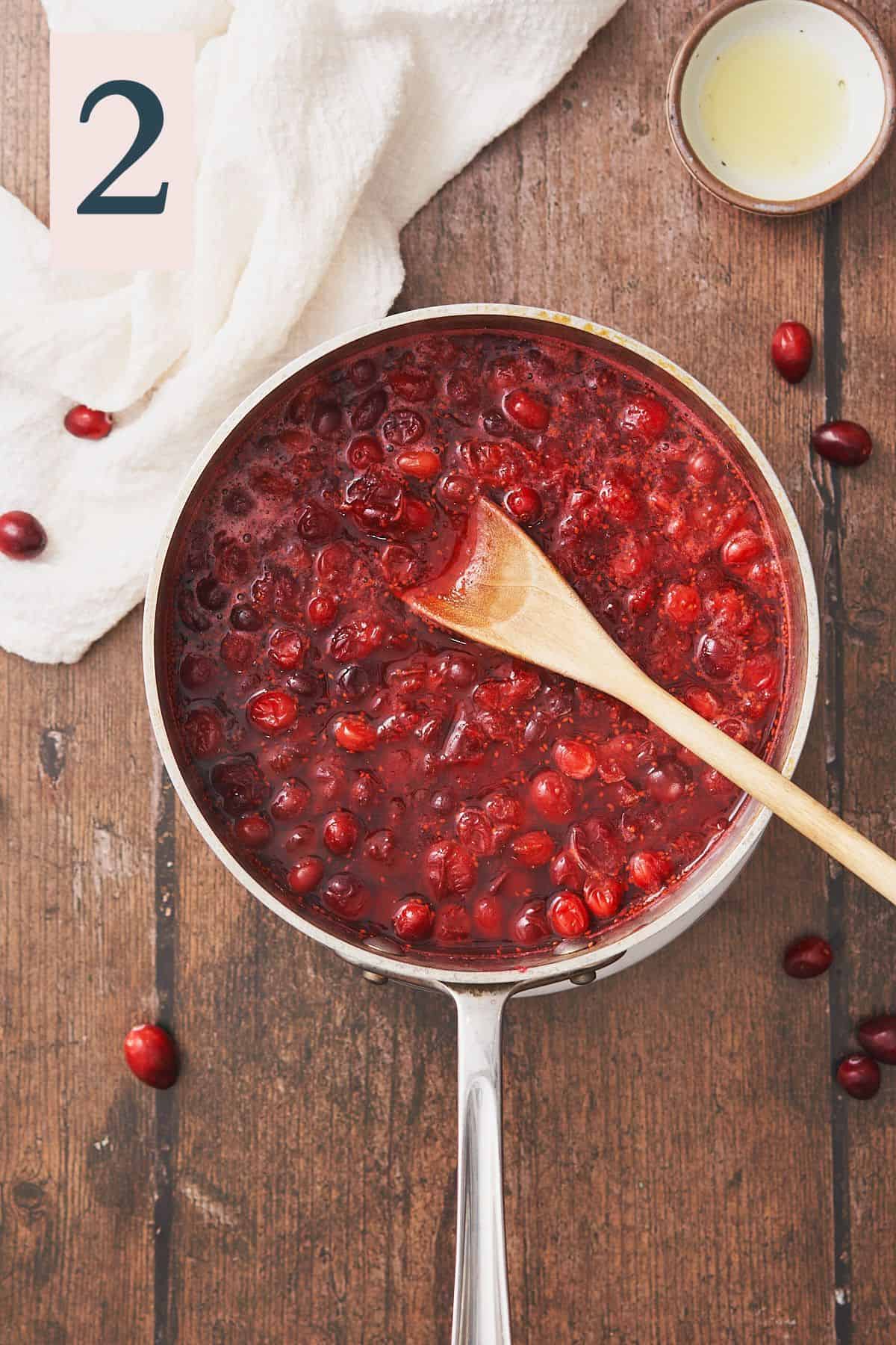 cranberries in a saucepan cooked down and softened, with a wooden spoon in the saucepan. 
