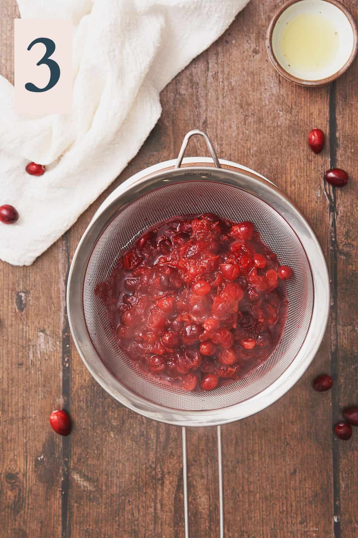 cranberries solids in a fine metal sieve over top of a saucepan. 