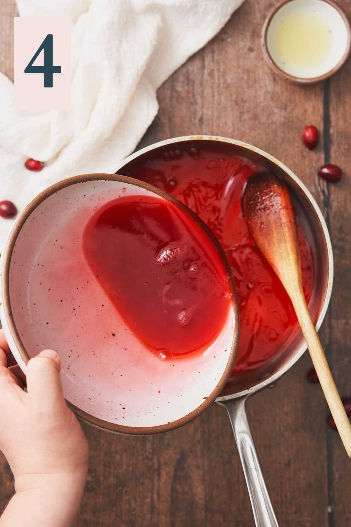 cranberry syrup in a ceramic bowl, with a hand pouring it back into a saucepan. 