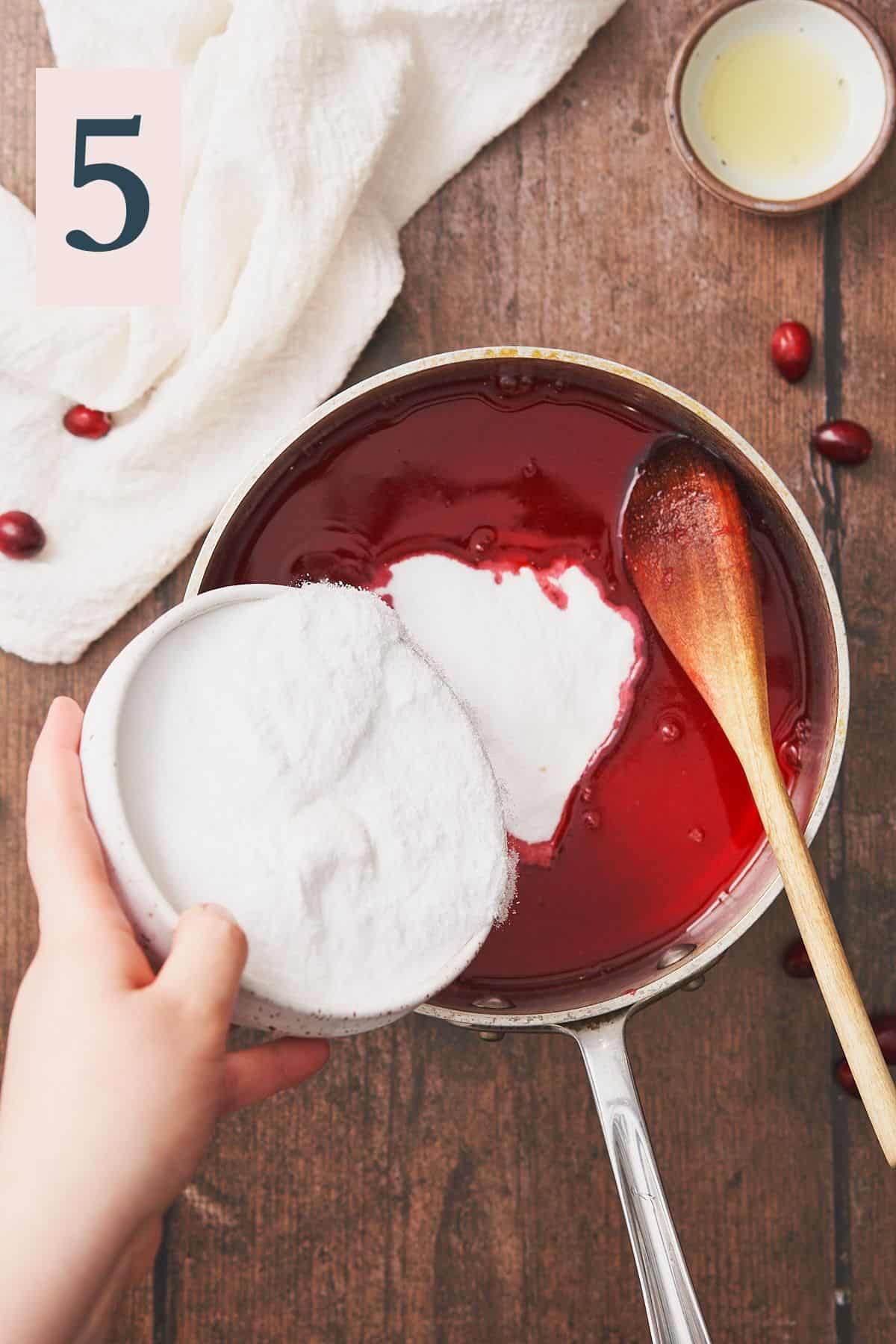 hand pouring sweetener into vibrant red cranberry simple syrup. 