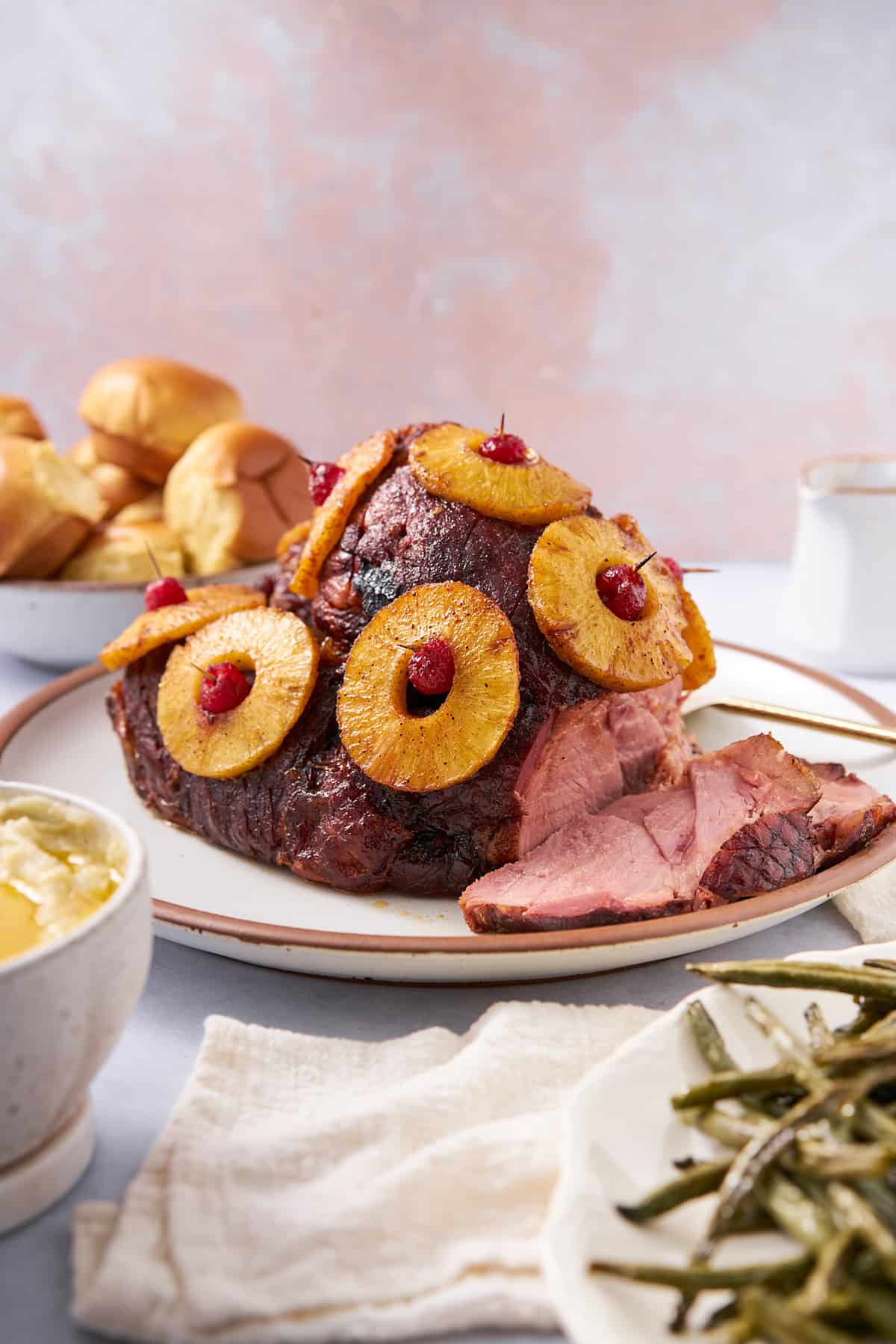 pineapple honey glazed ham with maraschino cherries, surrounded by rolls, and other sides.