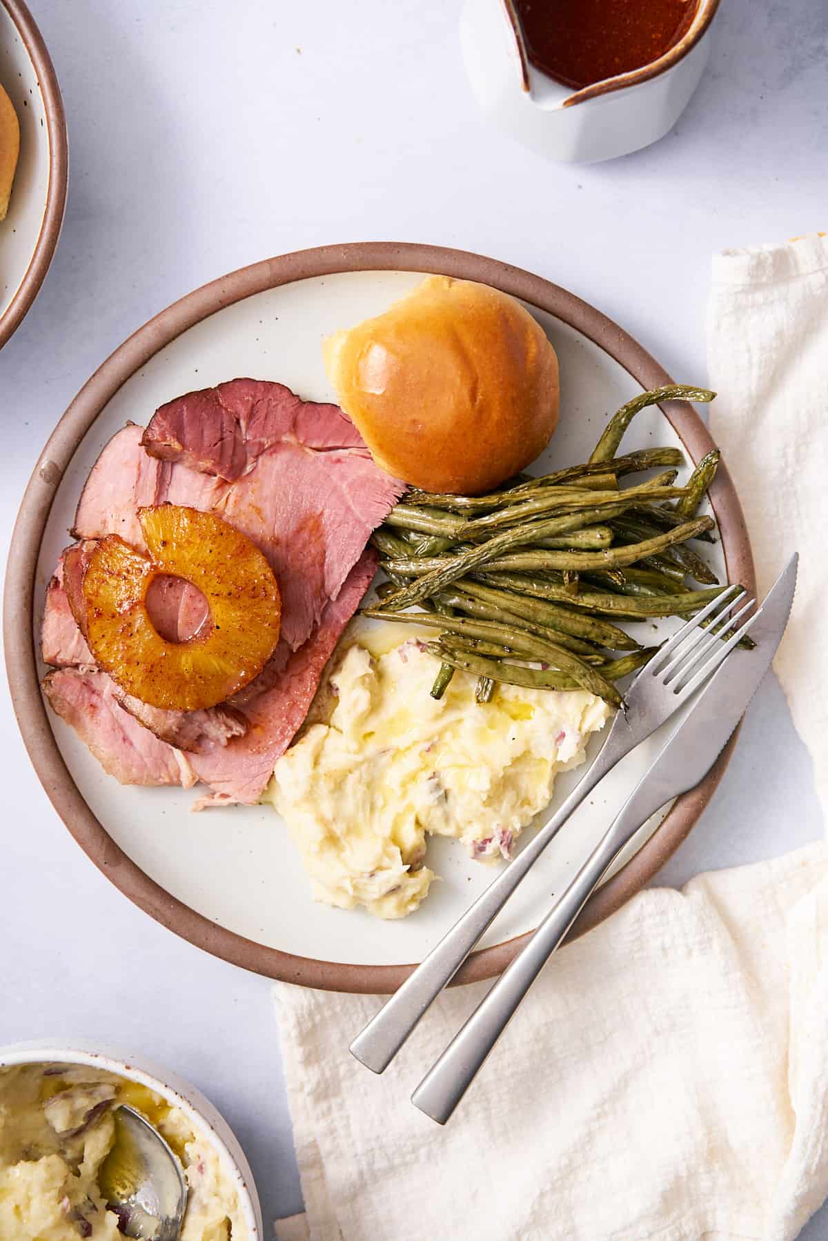 plate with rolls, green beans, and mashed potatoes with a slice of pineapple honey glazed ham.