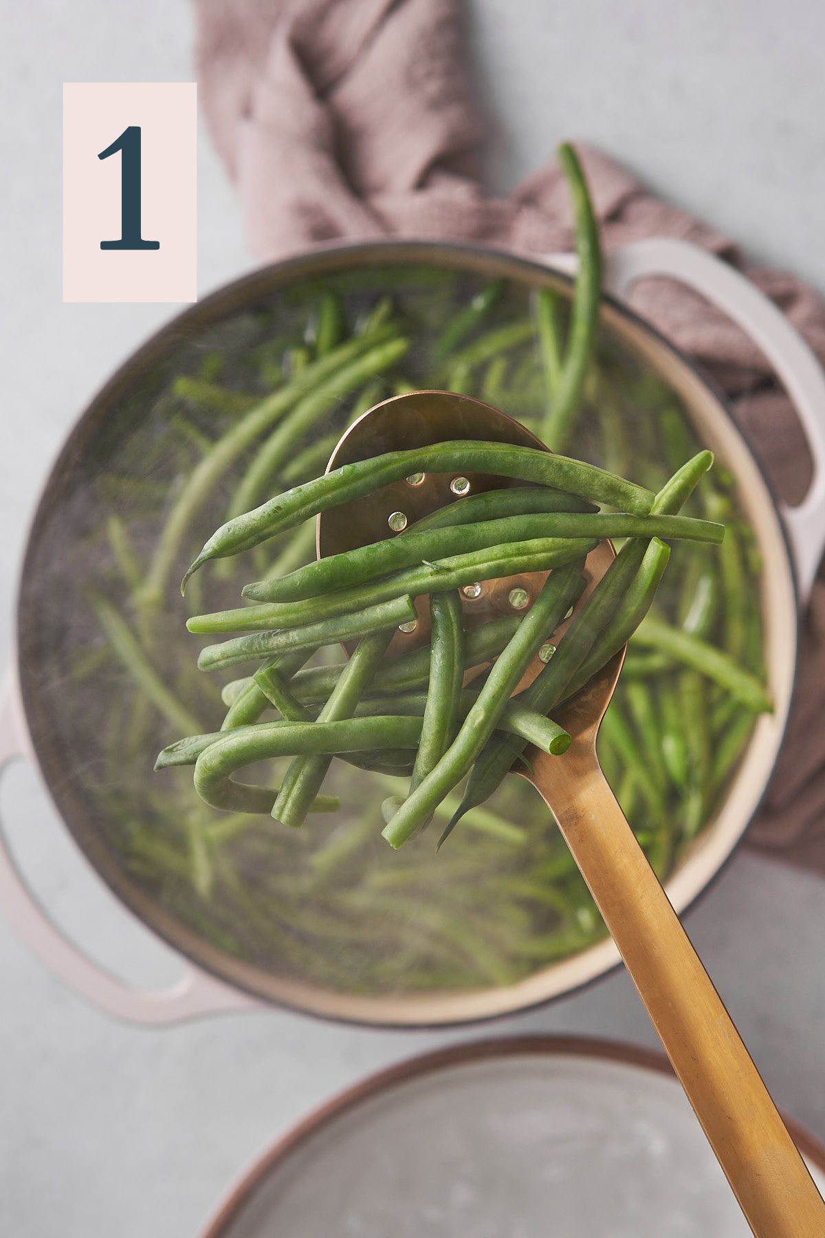 green beans above a large bot of boiling water, with a slotted spoon scooping them out of the pot. 
