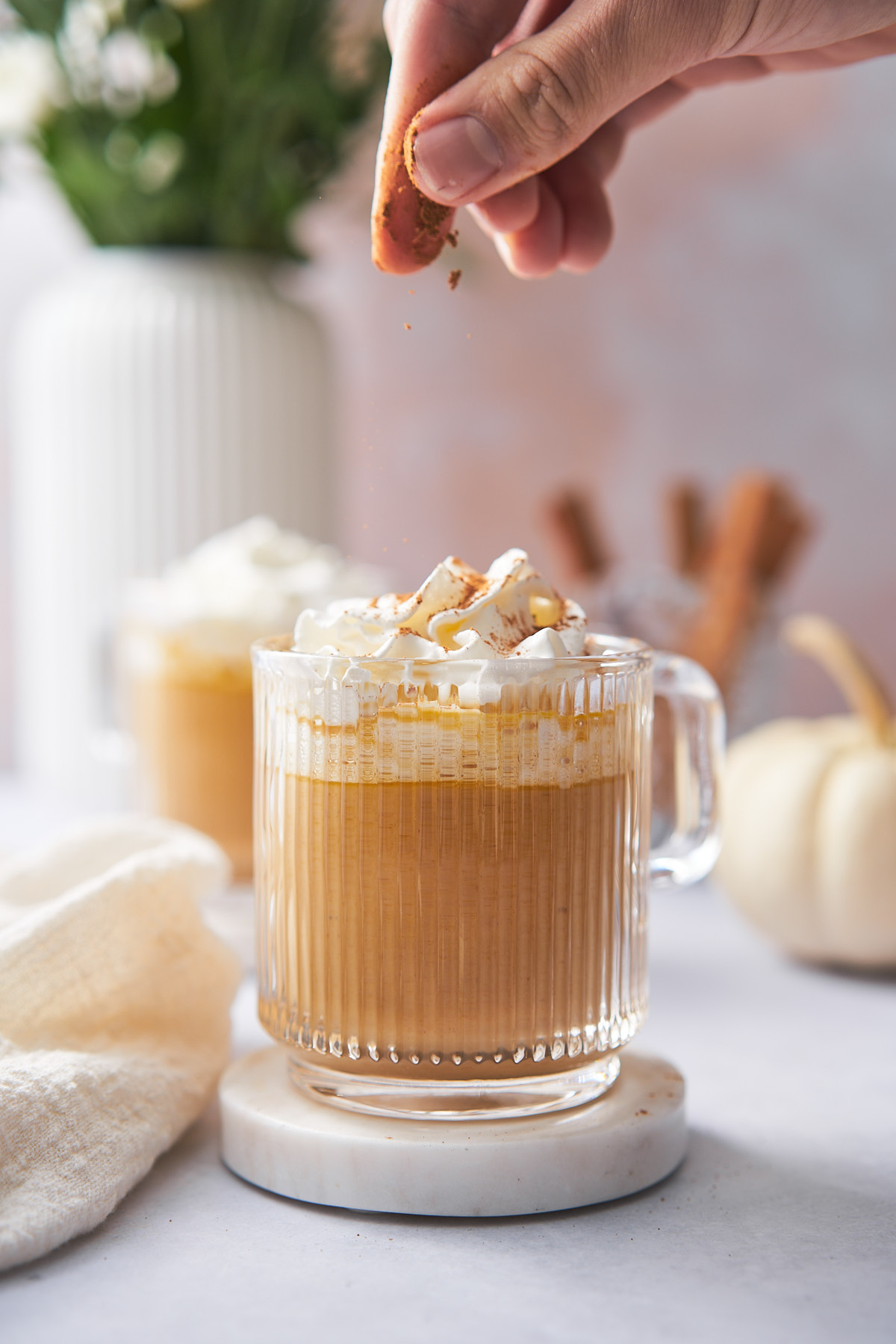 keto pumpkin spice latte topped with whipped cream and hand sprinkling pumpkin spice onto the top. 