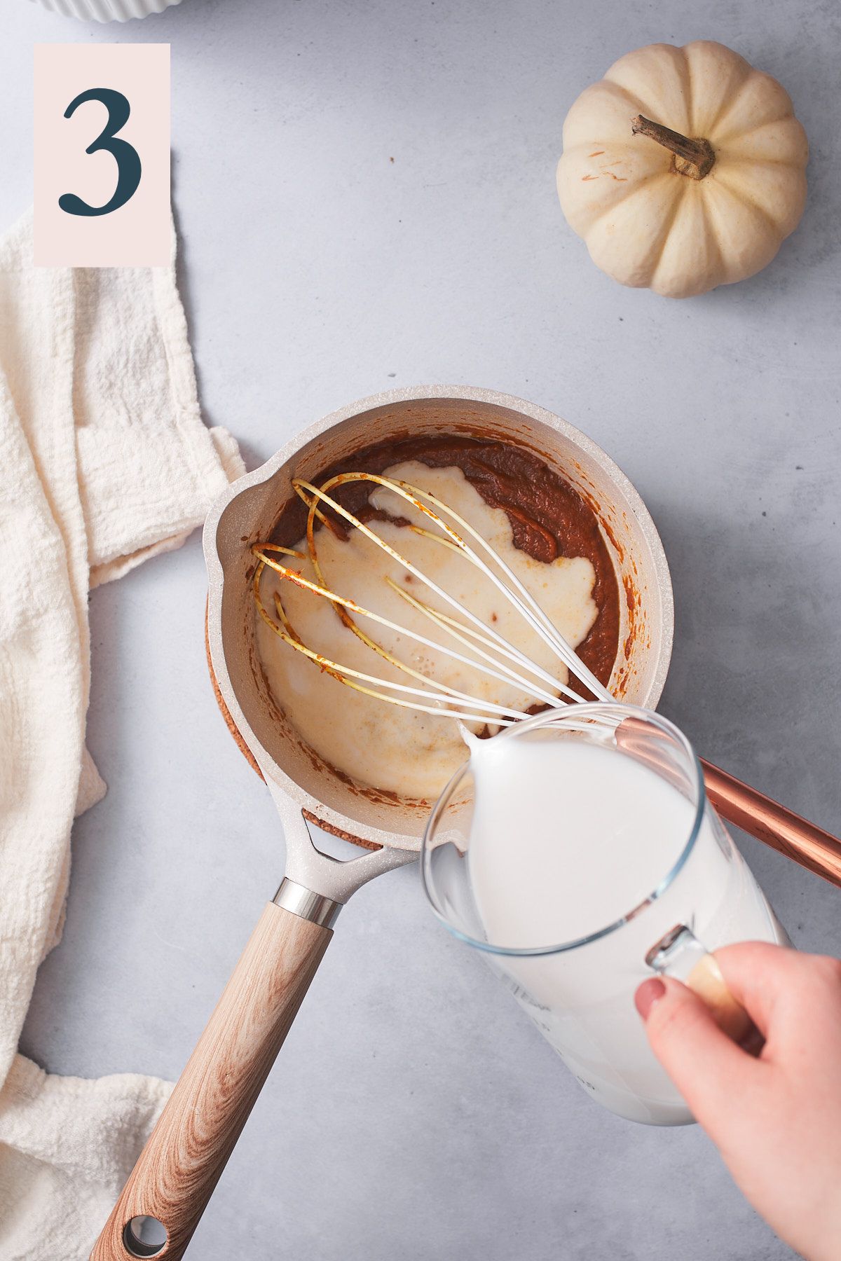 hand pouring nut milk over pumpkin puree mixture in a small saucepan. 