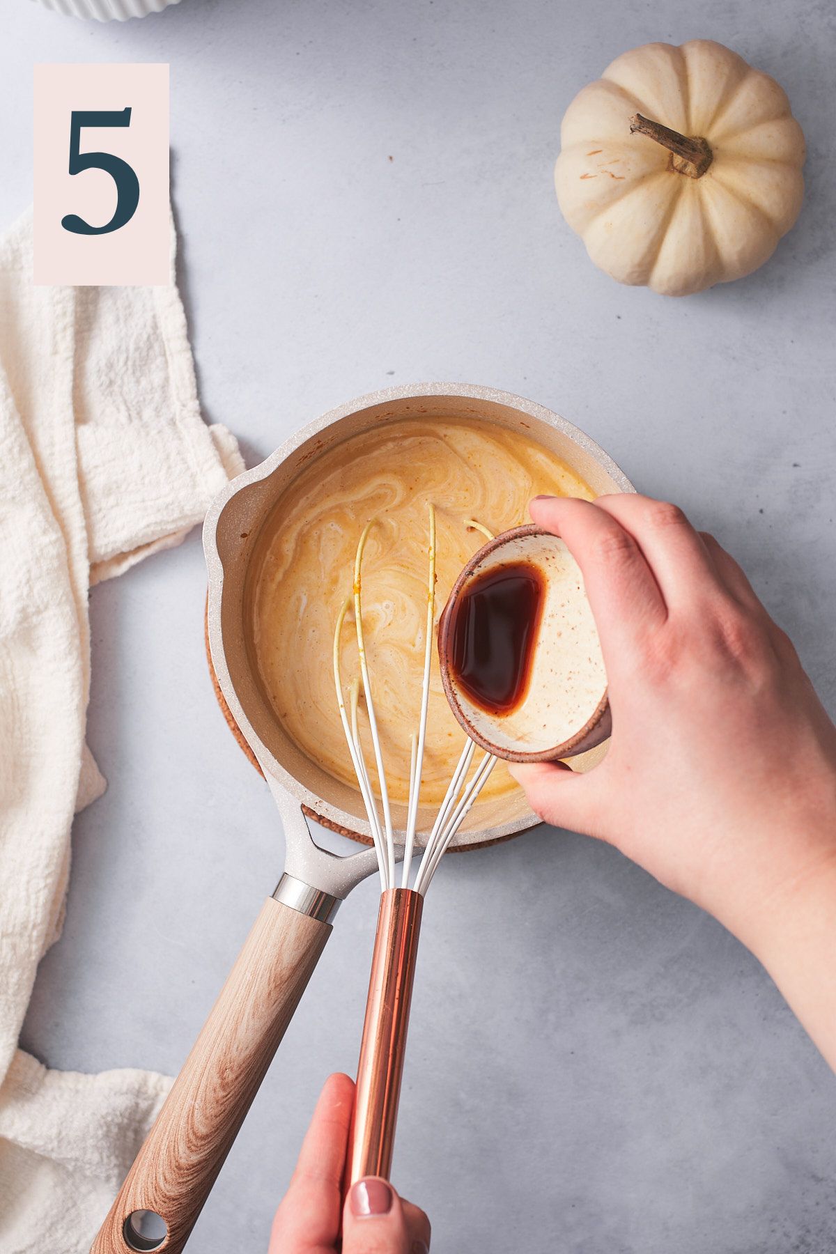 hand pouring vanilla extract into a saucepan with a pumpkin spice latte mixture.