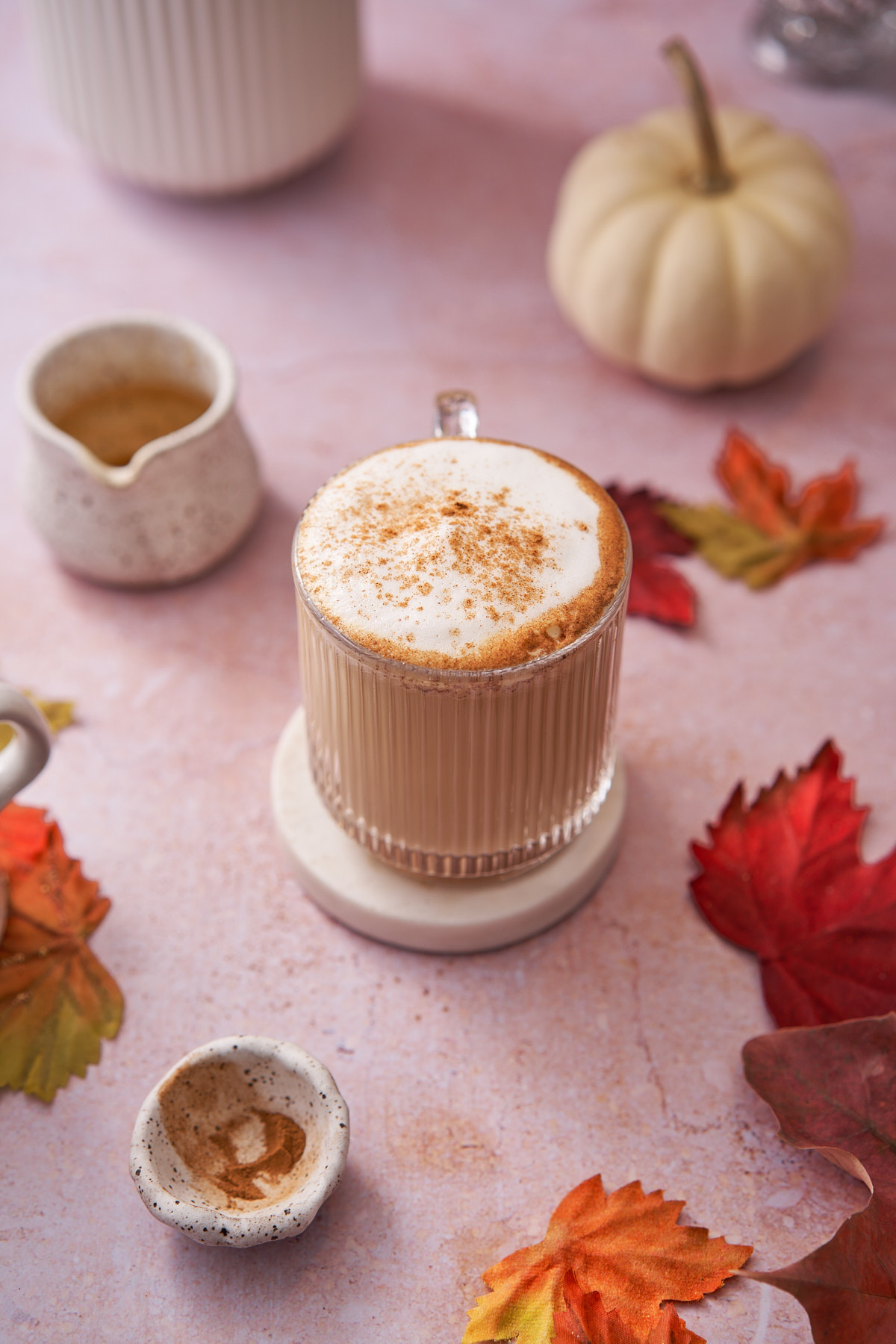 stunning maple latte surrounded by maple leaves, white pumpkins, and a small ceramic pitcher. 