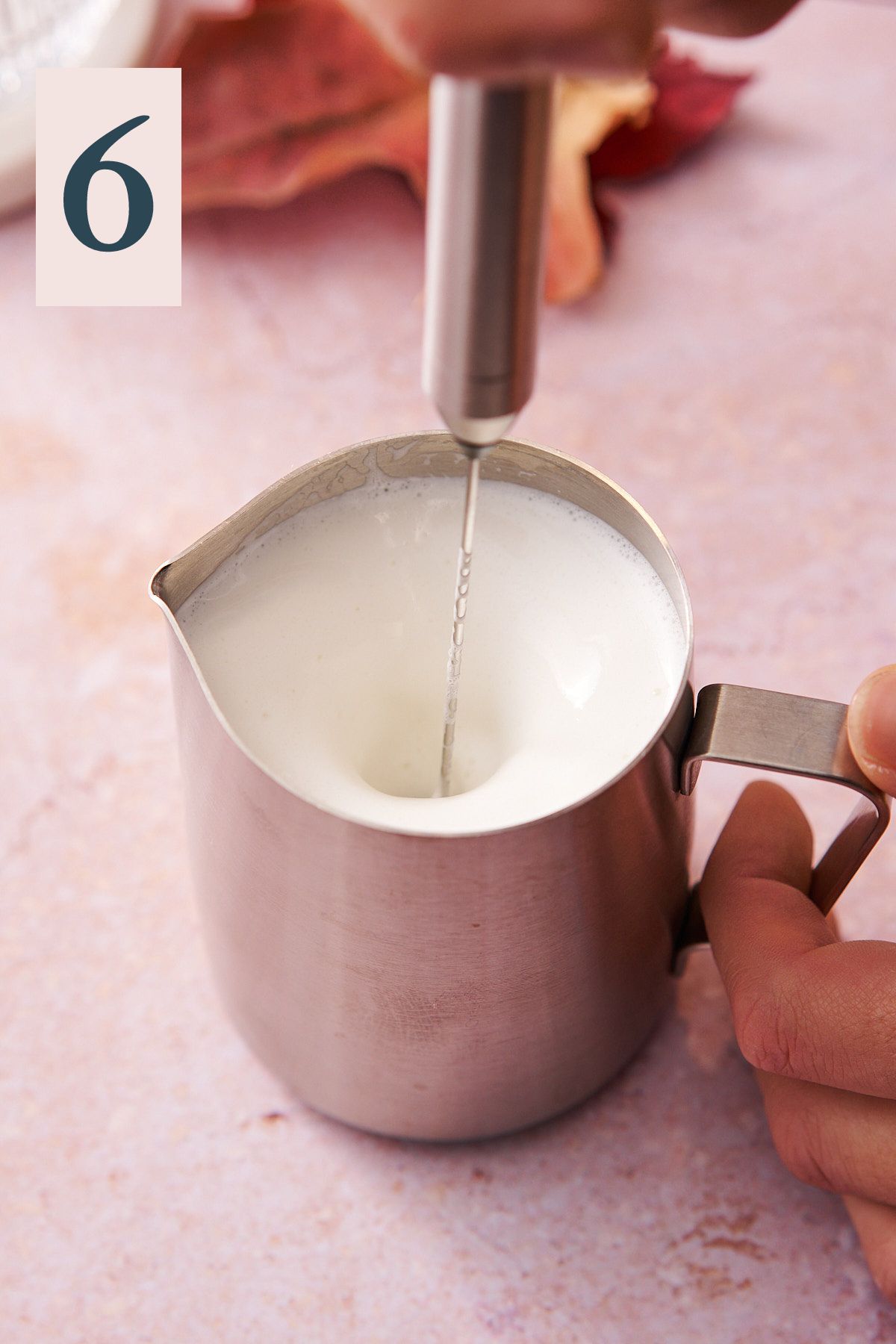 hand steaming milk with a milk frother in a metal pitcher. 