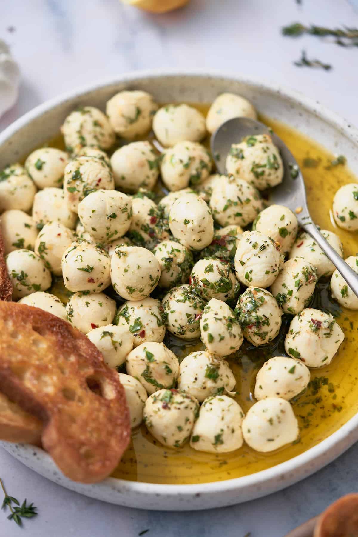plate full of marinated mozzarella bowls in olive oil with fresh herbs and crispy crostini. 