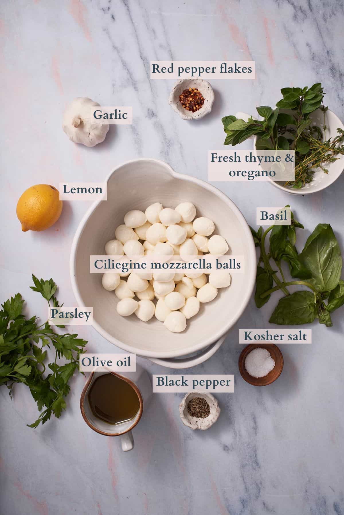 ingredients to make marinated mozzarella balls in ceramic bowls, with text overlaying to denote each ingredient. 