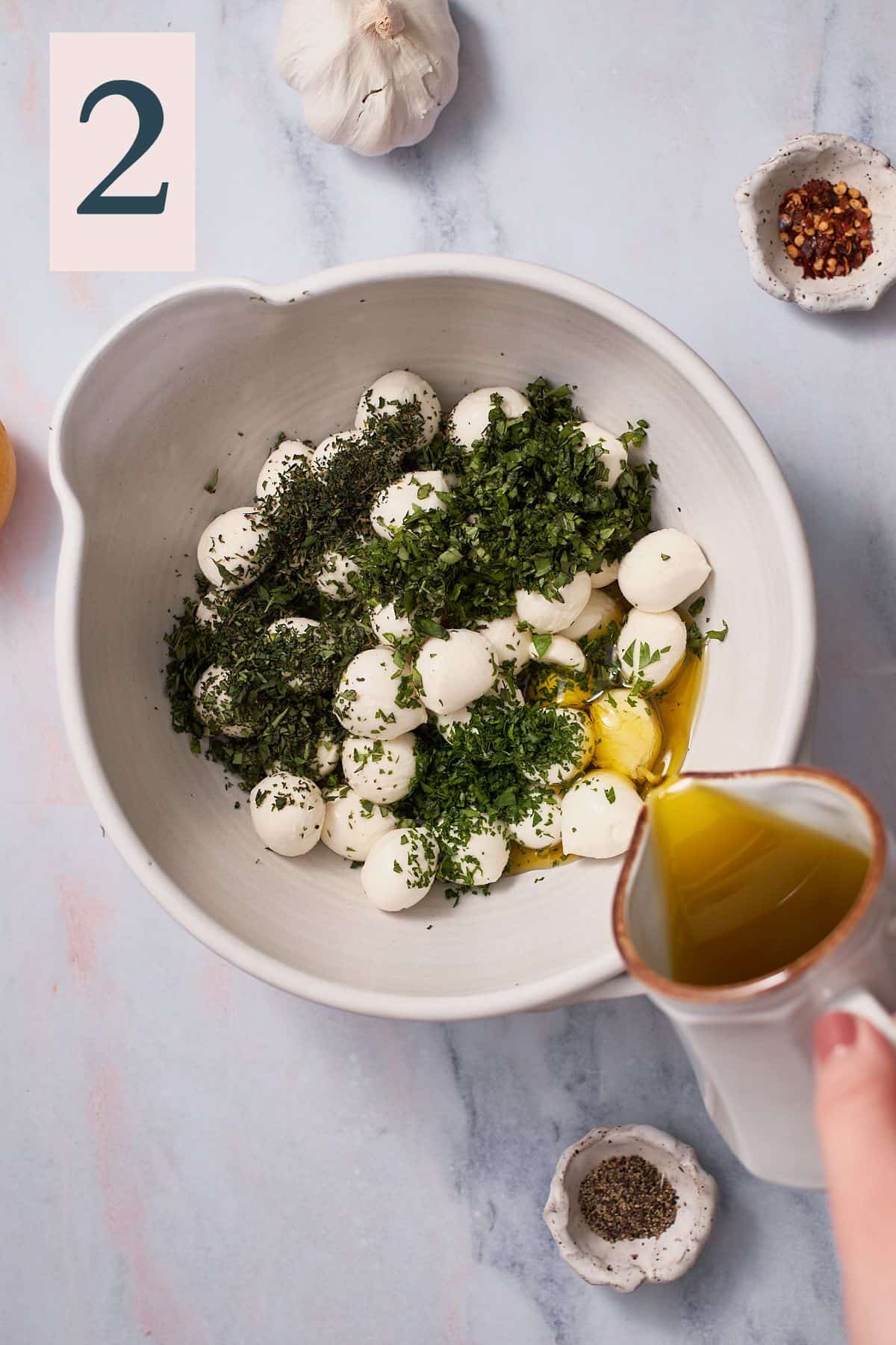 hand pouring olive oil into a bowl with mozzarella and herbs.