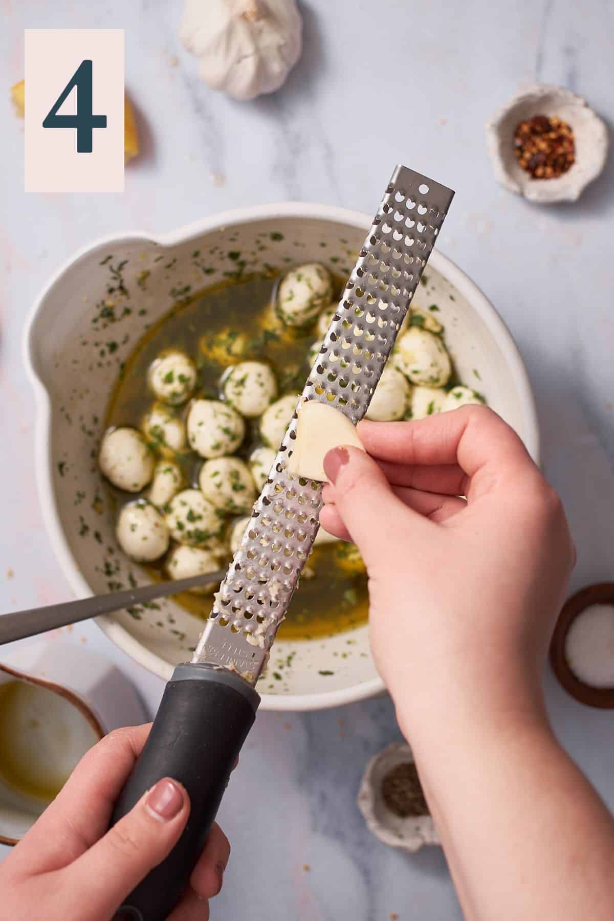 hand grating fresh garlic into a bowl with mozzarella balls, olive oil and fresh herbs. 