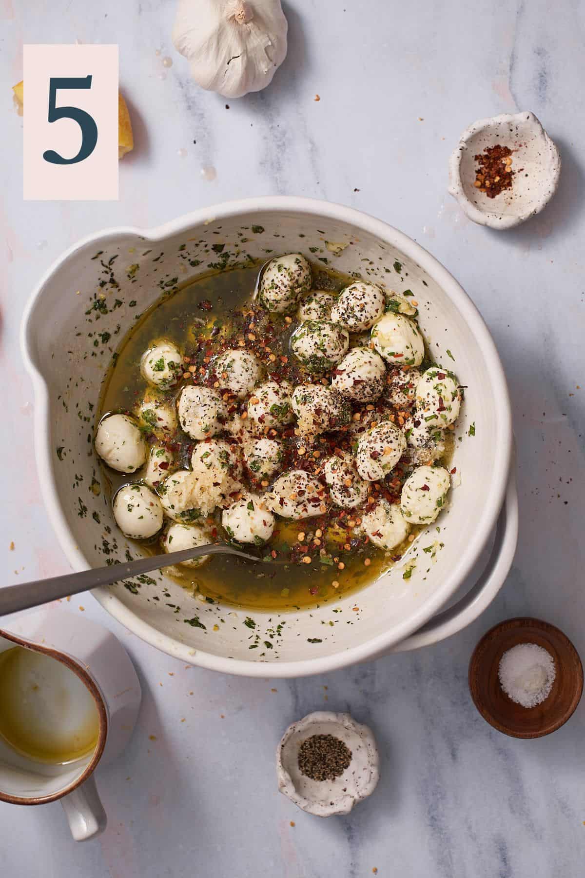 bowl of mozzarella balls with olive oil, herbs, red pepper flakes, black pepper and kosher salt in a bowl. 