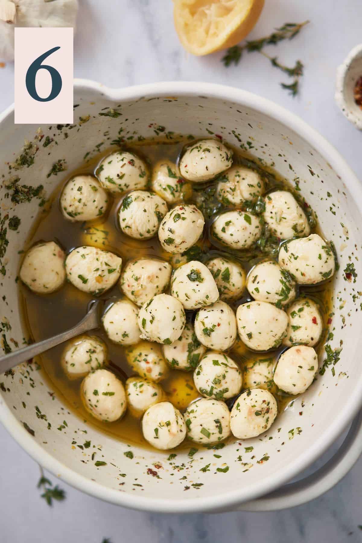 mozzarella balls in a white ceramic bowl, tossed with herbs and olive oil. 