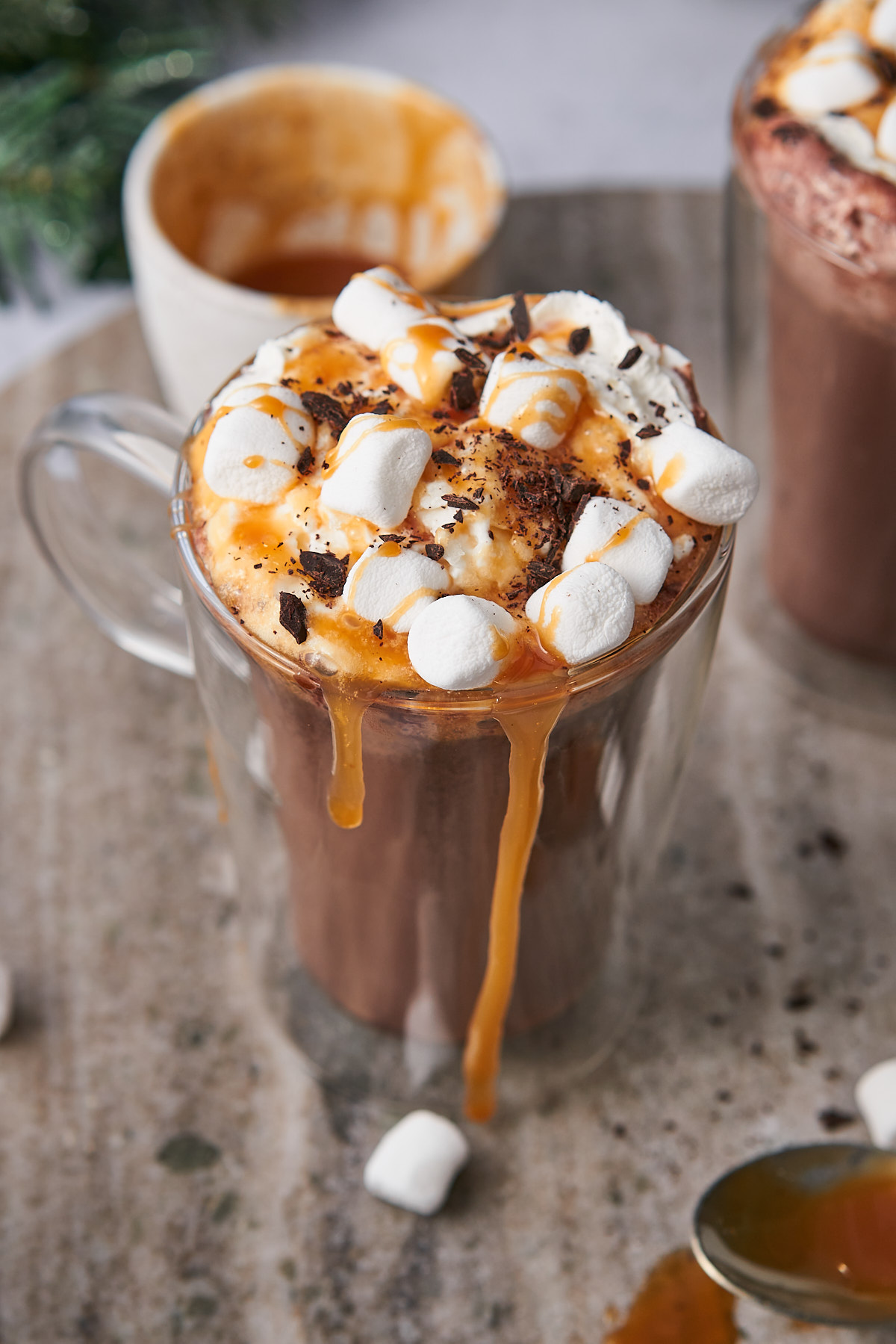 close up shot of a glass mug of salted caramel hot chocolate with marshmallows, whipped cream, caramel sauce, and chocolate shavings. 