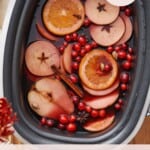 slow cooker mulled wine with orange slices, apple rounds, whole spices, and cranberries.