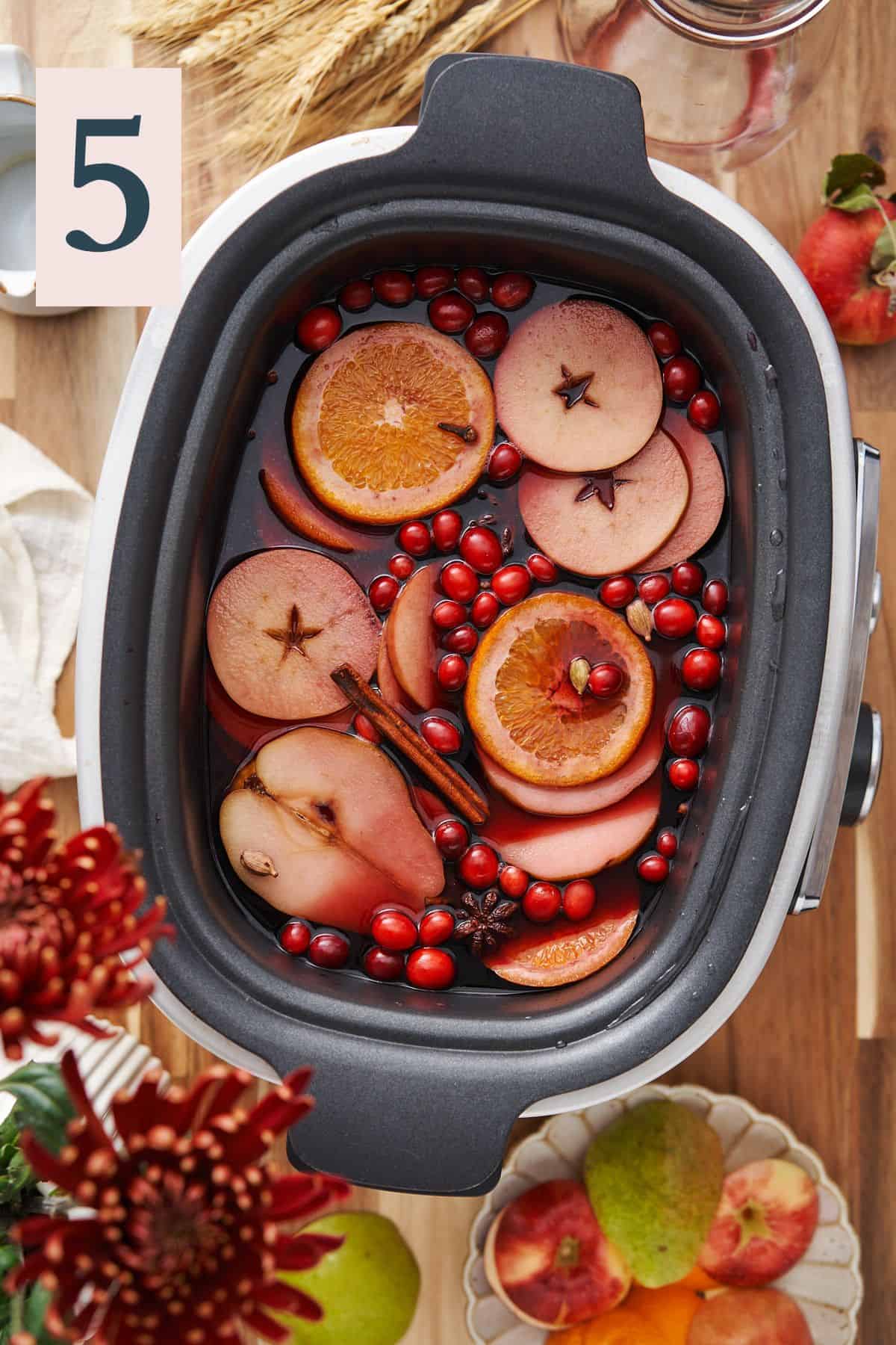 fruity red wine sangria in a slow cooker with whole spices, cranberries, oranges and apple slices. 