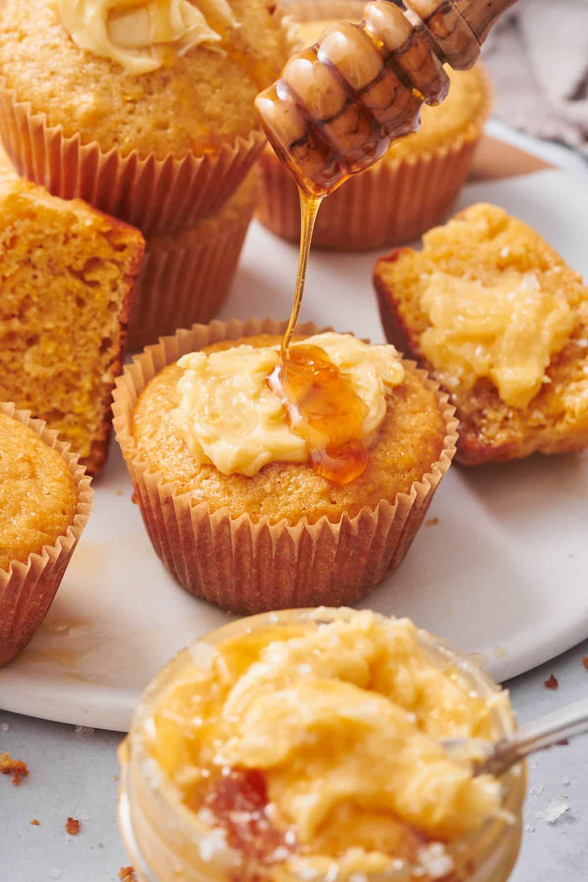 honey dripper drizzling on honey on top of a cornbread muffin with whipped honey butter. 