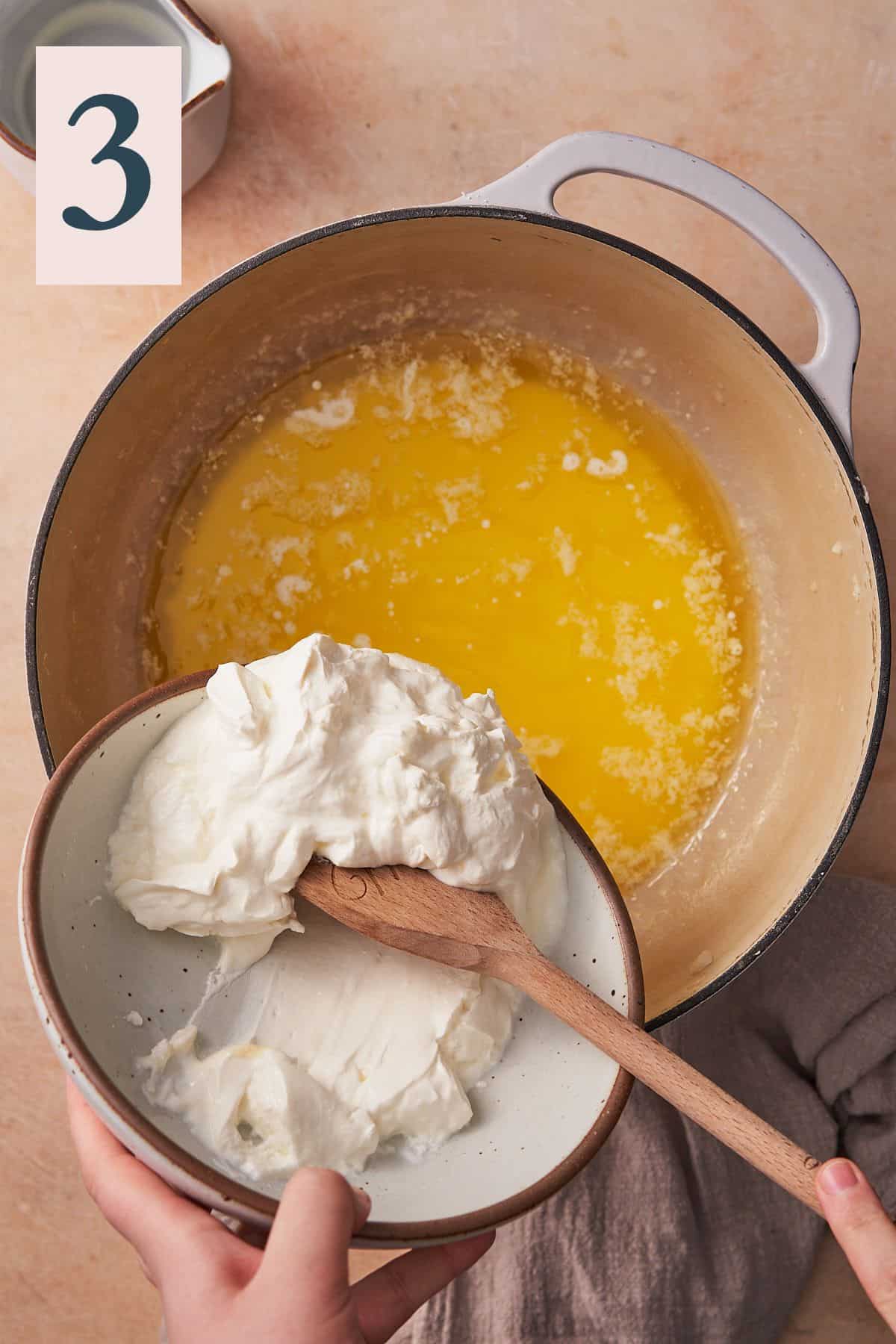 wooden spoon adding sour cream to a large pot of melted butter and cream.