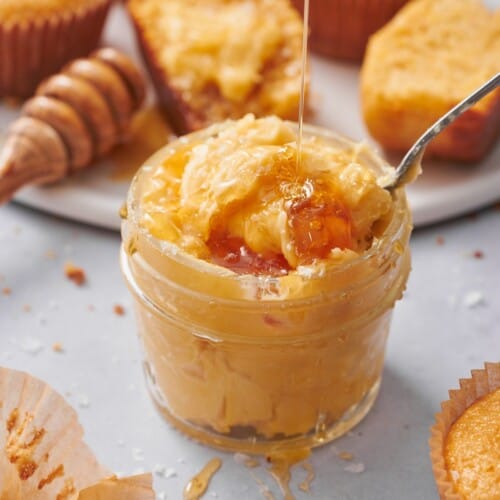 whipped honey butter topped with flaky sea salt and being drizzled with honey, with cornbread muffins on the scene.