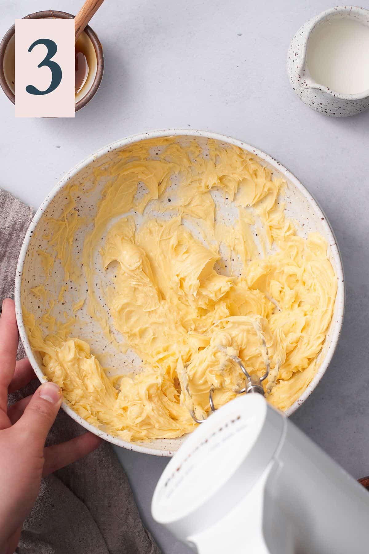 hand holding a cordless hand mixer and mixing butter. 