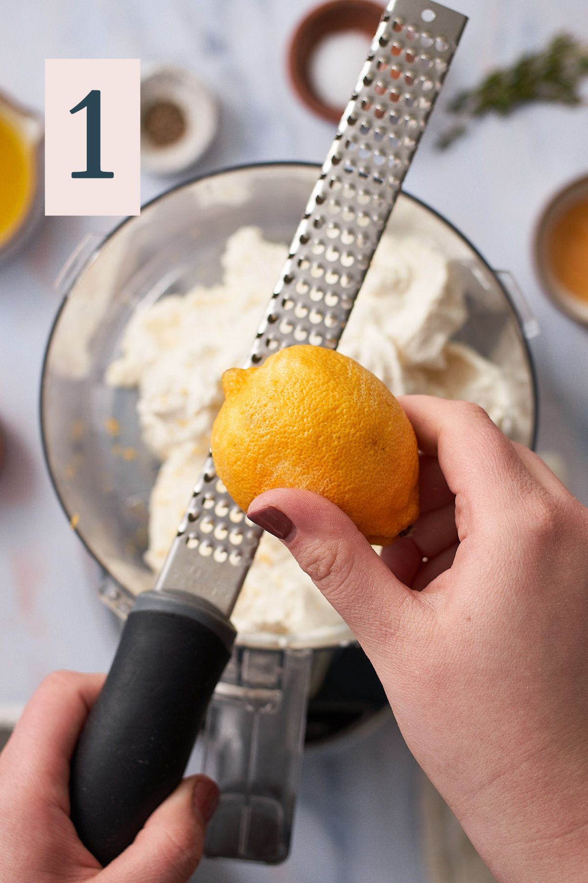 hand grating lemon zest into a food processor with ricotta cheese. 