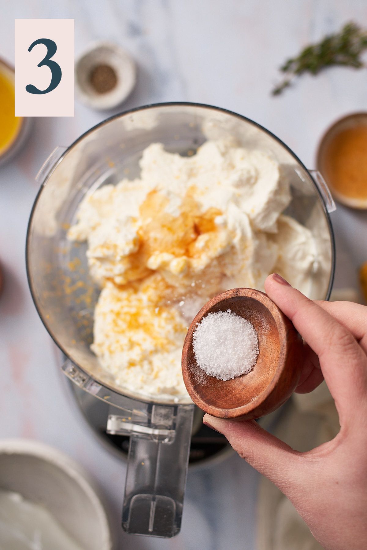 hand shaking kosher salt into a food processor with ricotta, honey, and lemon zest.