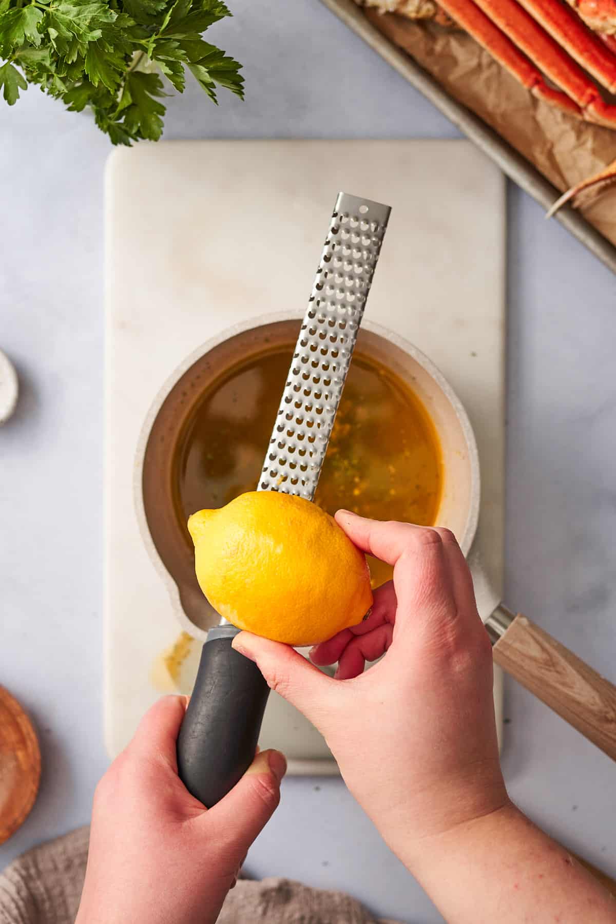 Hand zesting a lemon into a buttery sauce in a saucepan.
