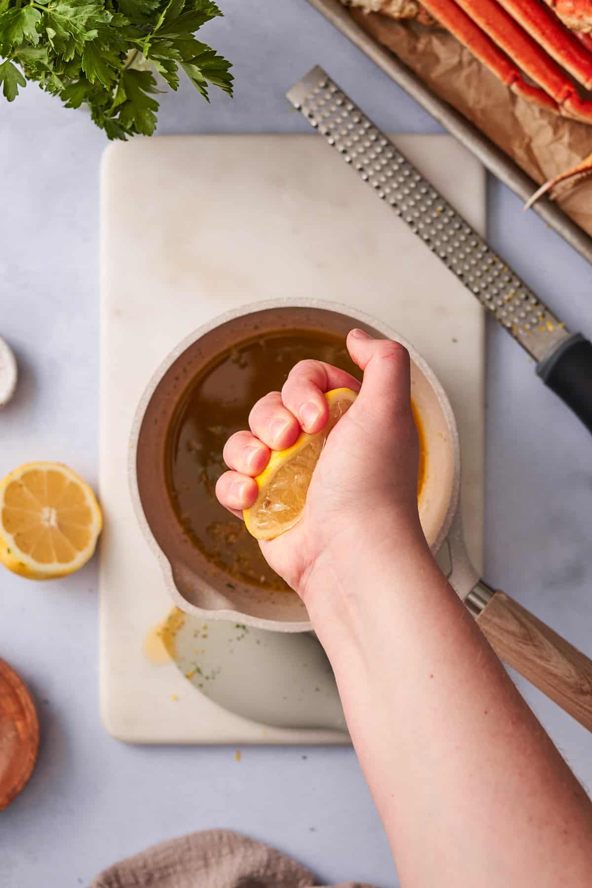 Hand squeezing lemon juice in a sauce pan of garlic butter.