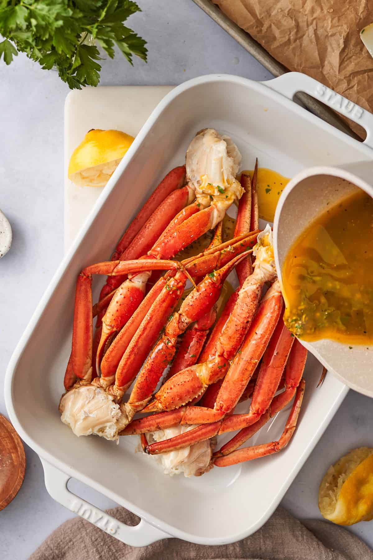 Pouring garlic butter sauce over baked crab legs in a casserole dish.