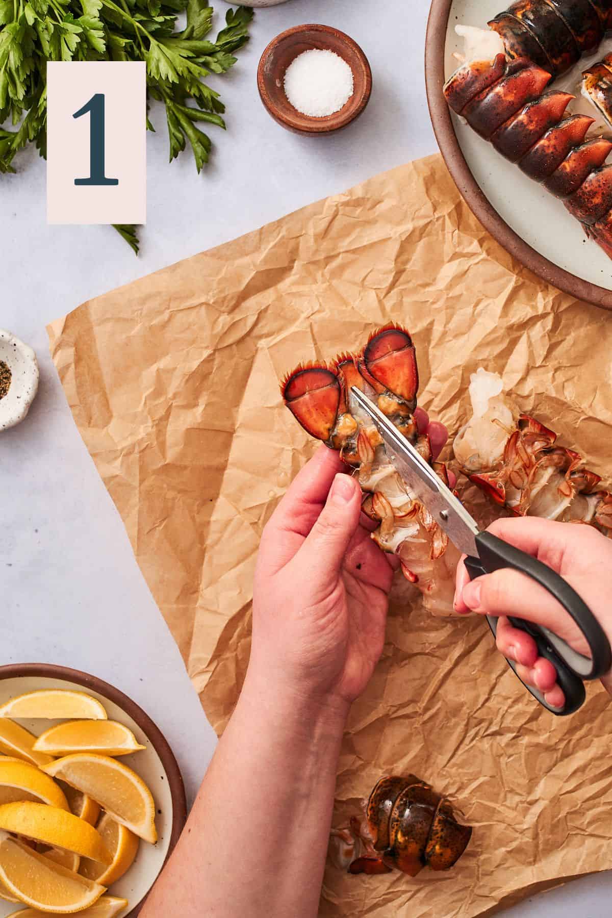 hand cutting lobster from the underside with a pair of kitchen shears, with parchment paper underneath. 
