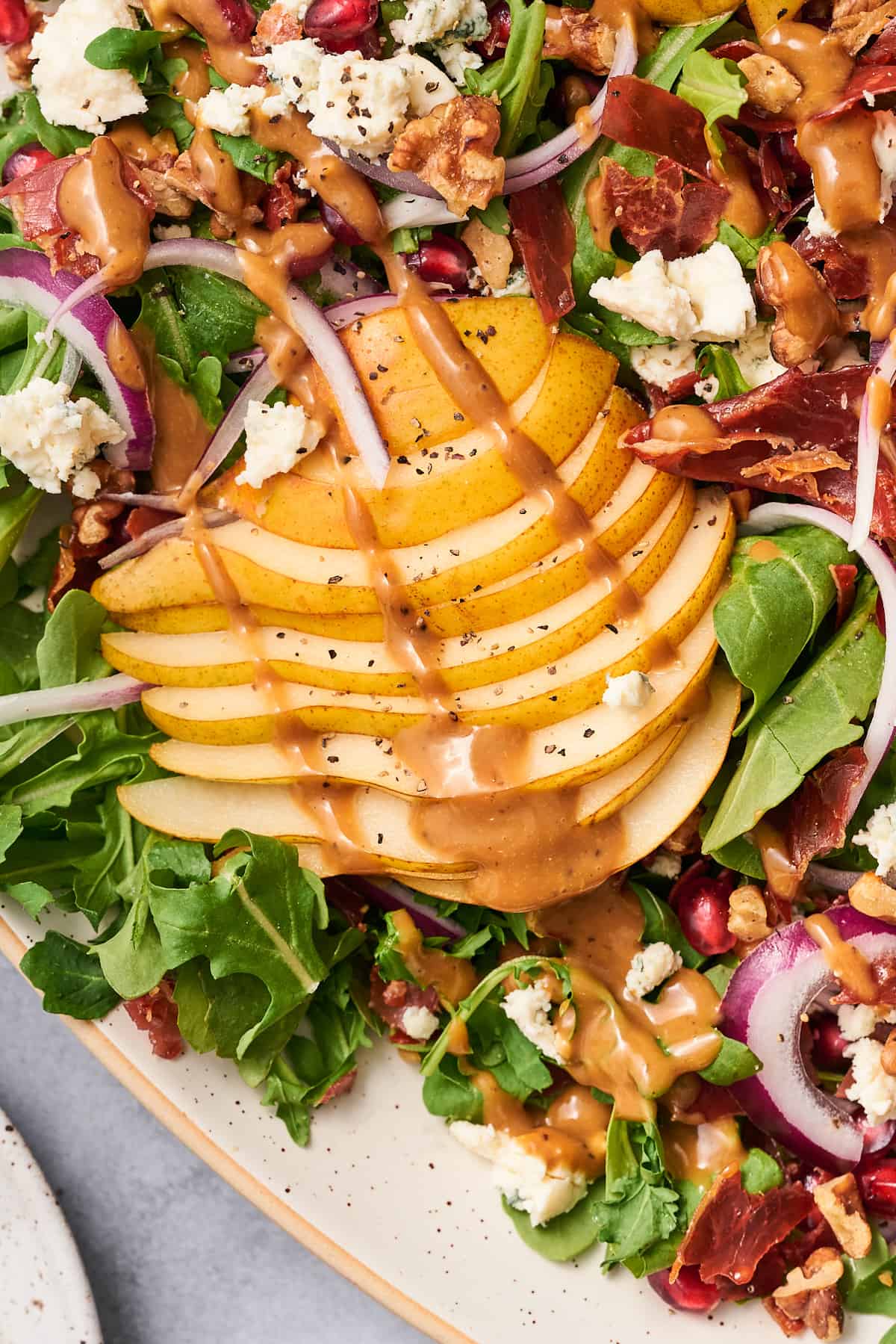 creamy balsamic dressing drizzled over top of a pear arugula salad with pomegranates and blue cheese.