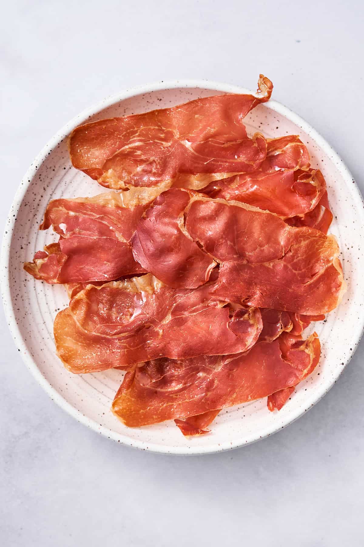 crispy prosciutto on a white ceramic plate on a grey backdrop. 