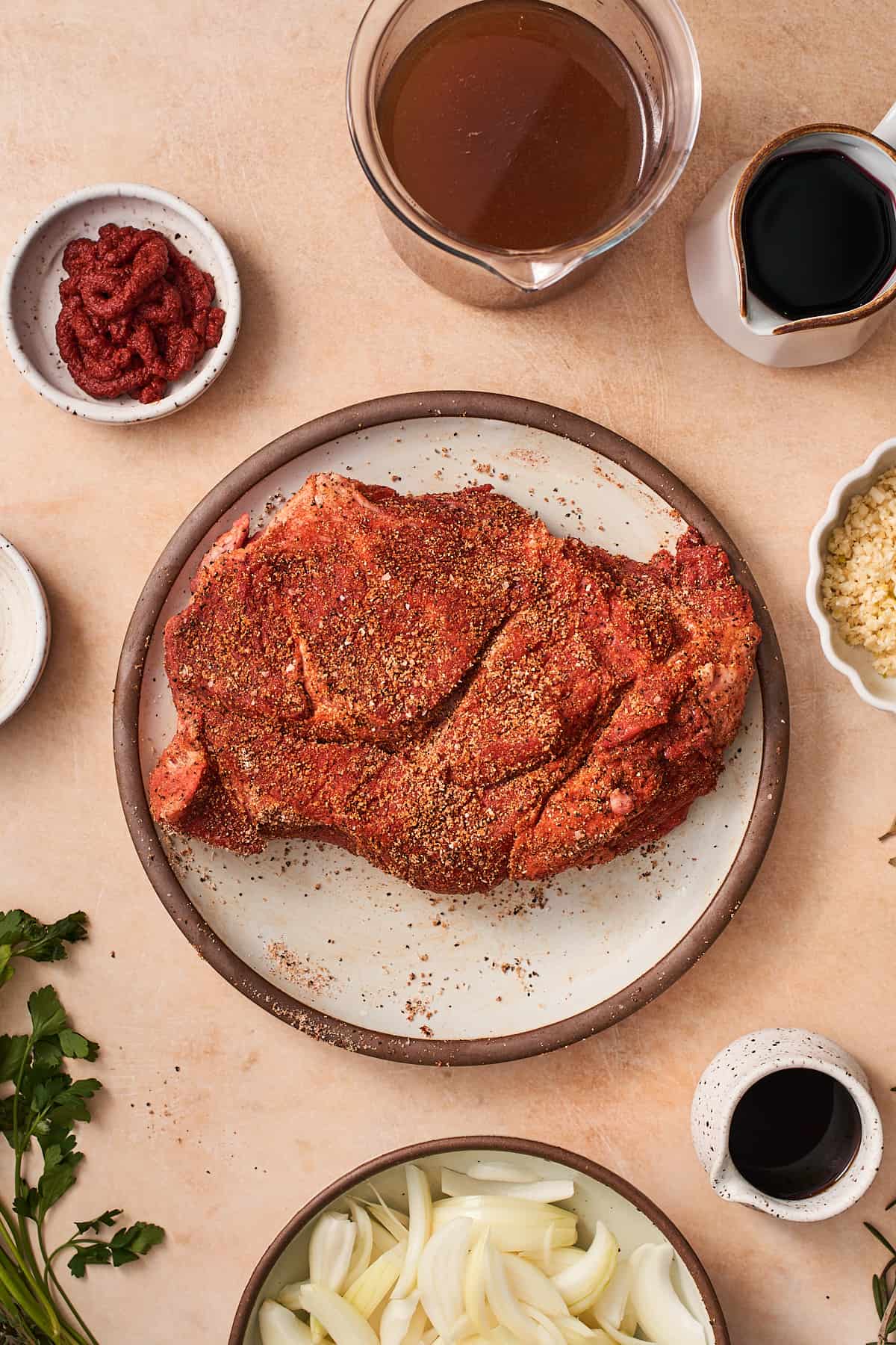 piece of chuck roast seasoned with salt, pepper, garlic power, onion powder, and smoked paprika on a plate.