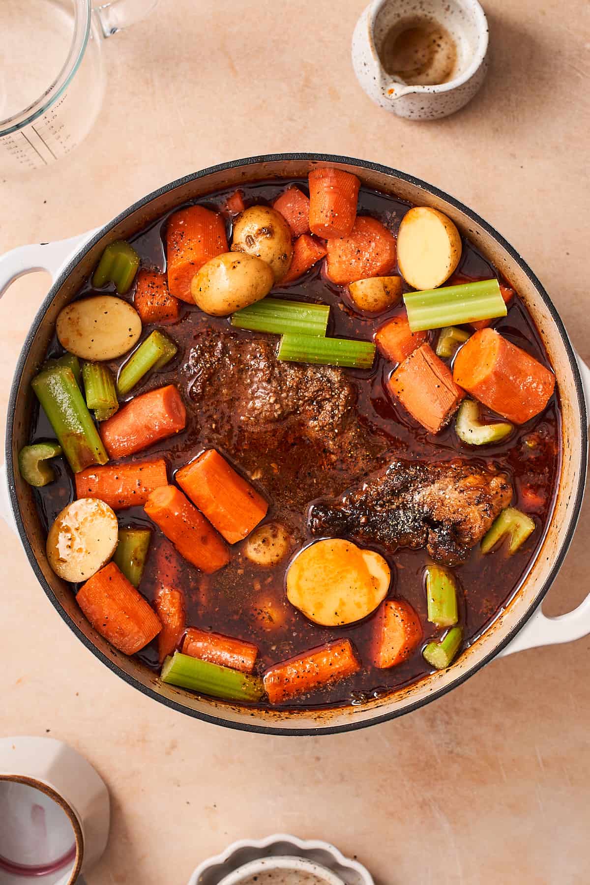 pot roast in braising liquid, with potatoes, celery and carrots added to the pot.