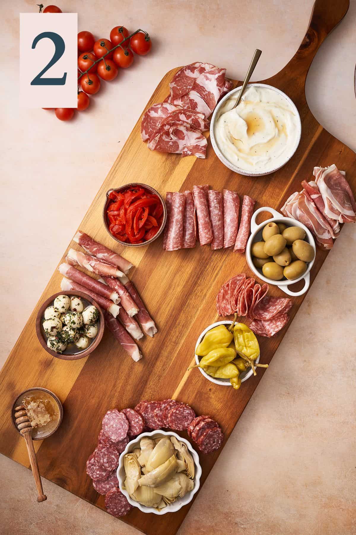 wooden board with peppers, olives, meats, and cheeses. 