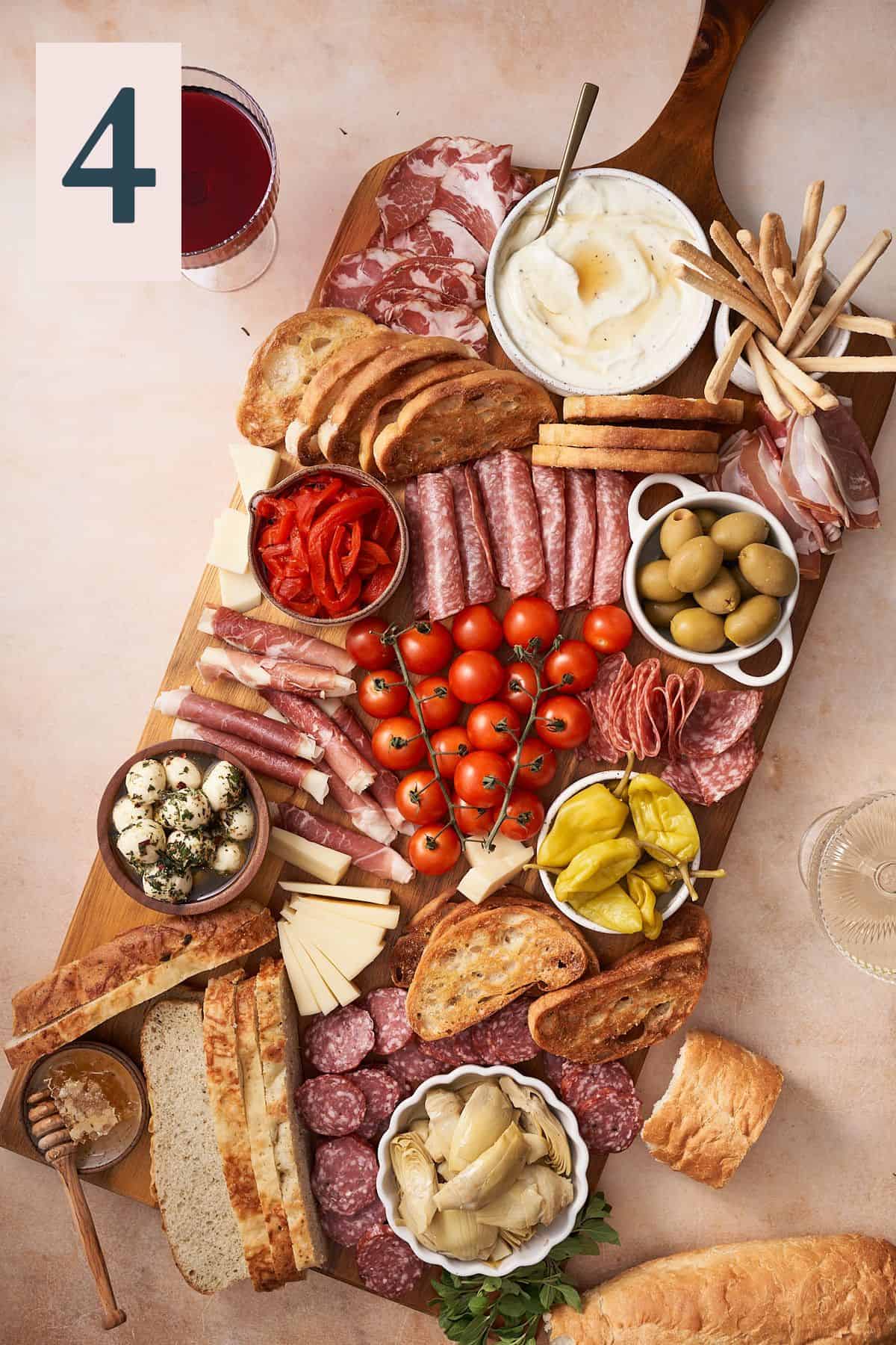 italian antipasto platter on a large wooden board, with an assortment of Italian meats, cheeses, tomatoes, olives, peppers, breads, and crackers. 
