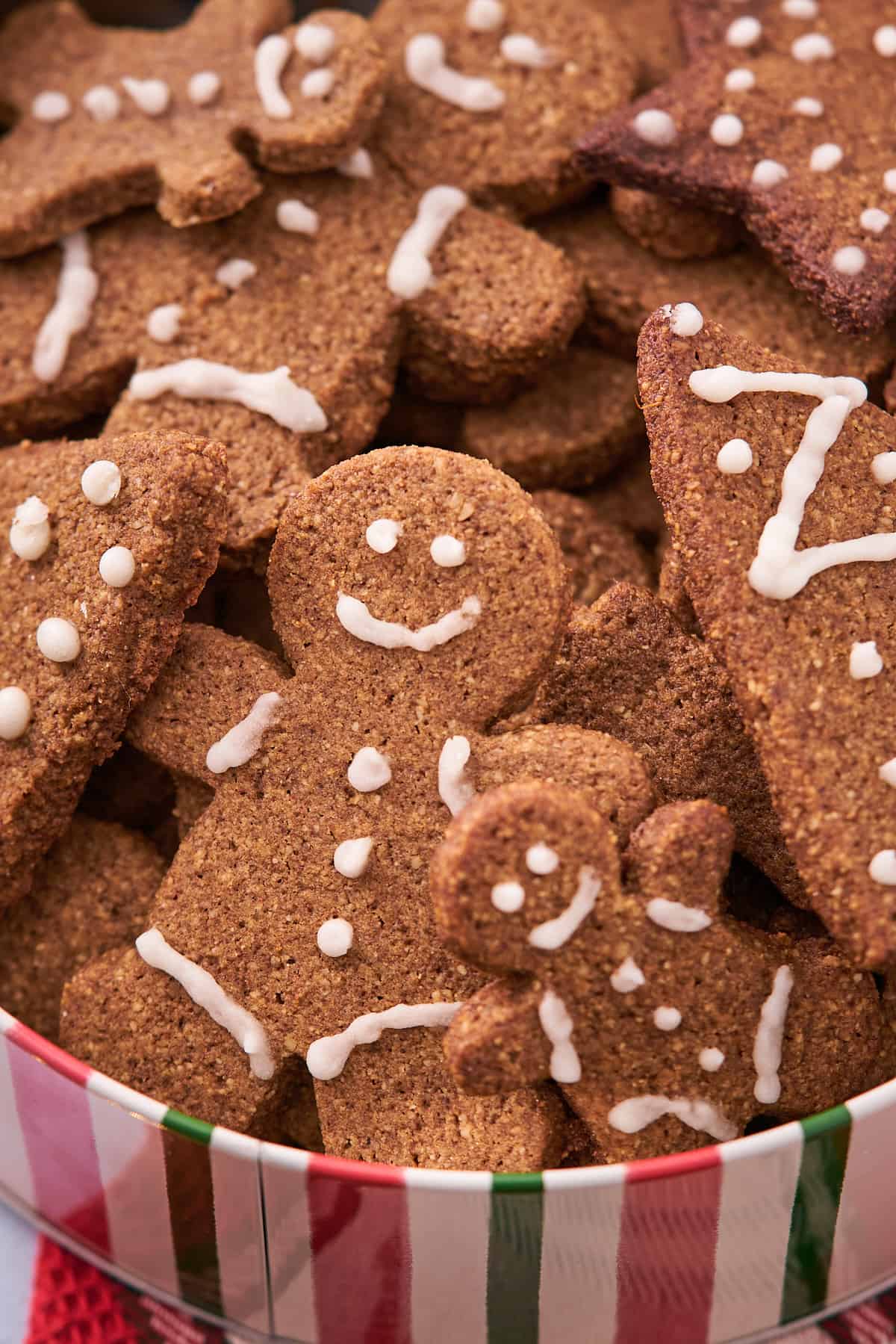super cute keto gingerbread cookies in a metal christmas cookie tin, decorated with white icing. 