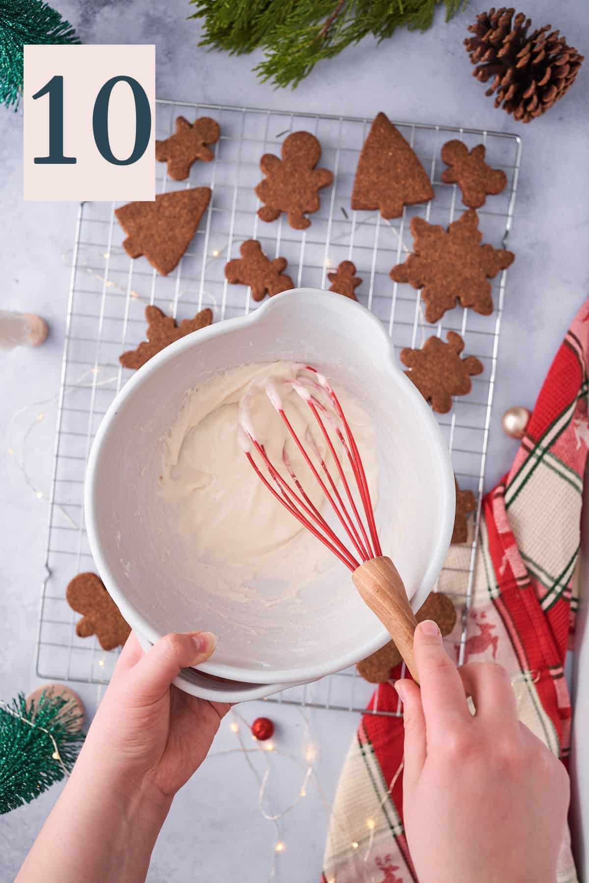 hand mixing together icing in a small bowl over cooling gingerbread cookies.