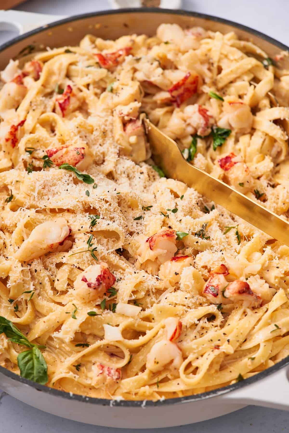 macro shot of creamy lobster pasta with chunks of lobster meat, basil, and thyme. 