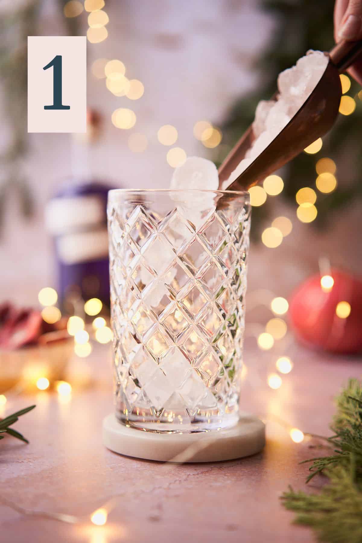 using a rose gold ice scooper to add ice to a cocktail shaker, with twinkling lights, pomegranate, and balsam in the background.